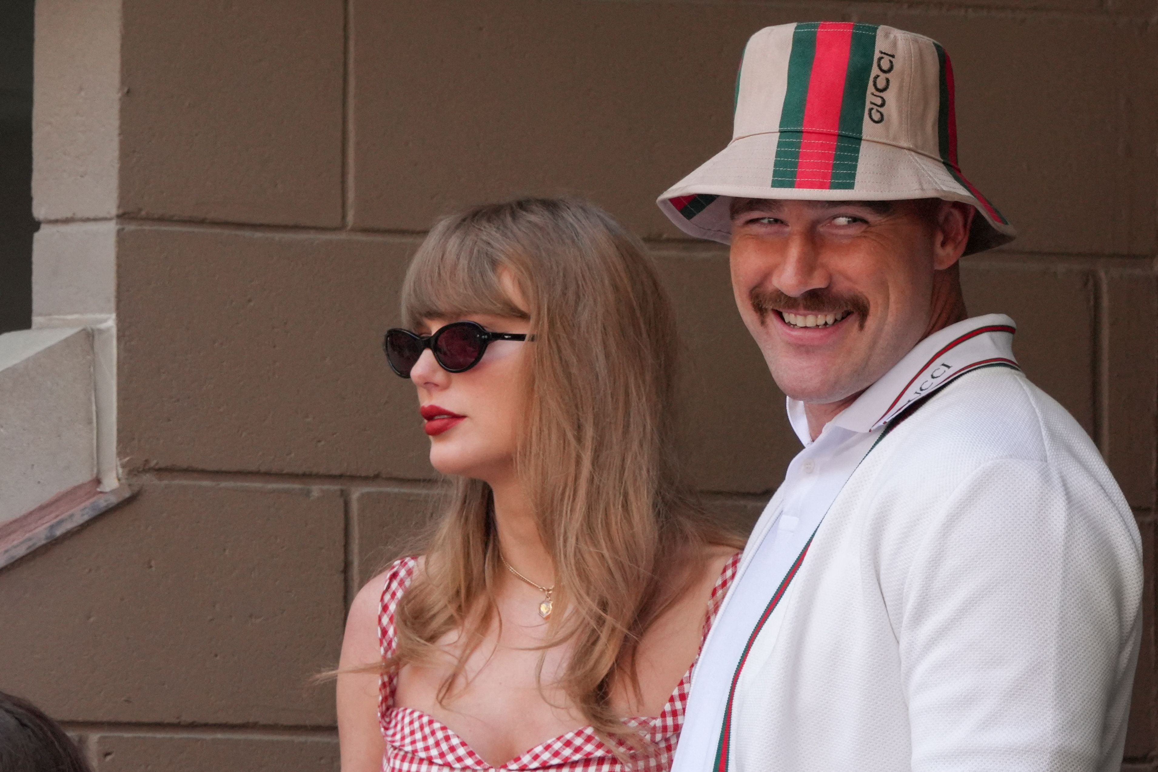 Eine Frau mit Sonnenbrille und ein Mann mit Gucci-Hut stehen nebeneinander und lächeln.