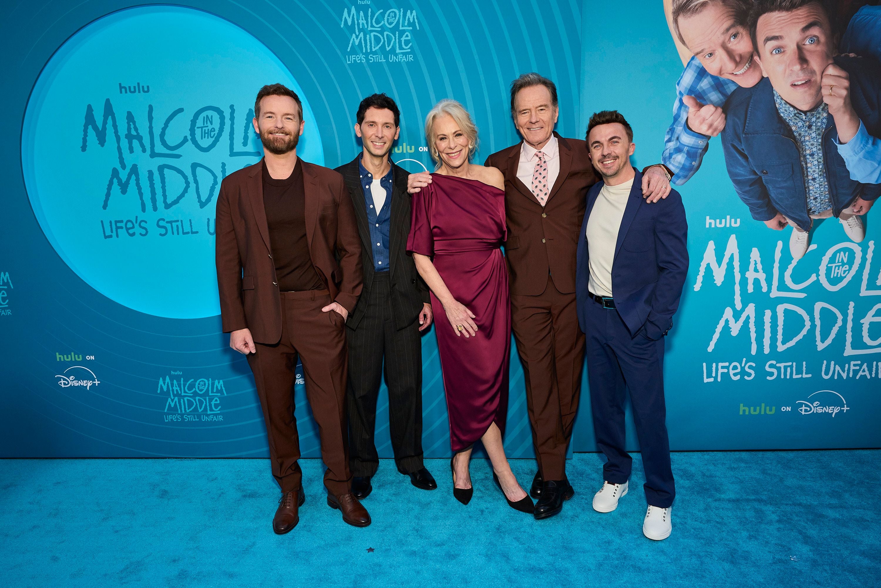 Fünf Personen posieren lächelnd vor einem „Malcolm in the Middle“-Premieren-Backdrop.