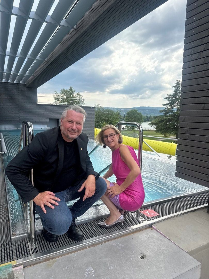 Ein Mann und eine Frau posieren lächelnd am Beckenrand eines überdachten Pools.