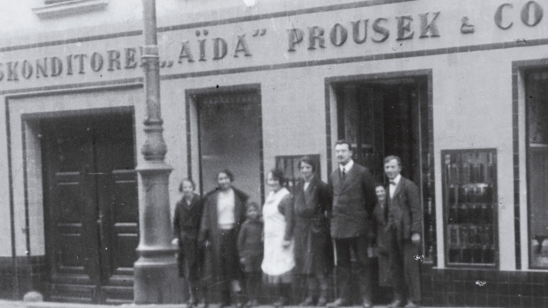 Schwarzweißfoto von sieben Menschen vor der Konditorei "Aïda" Prousek & Co.