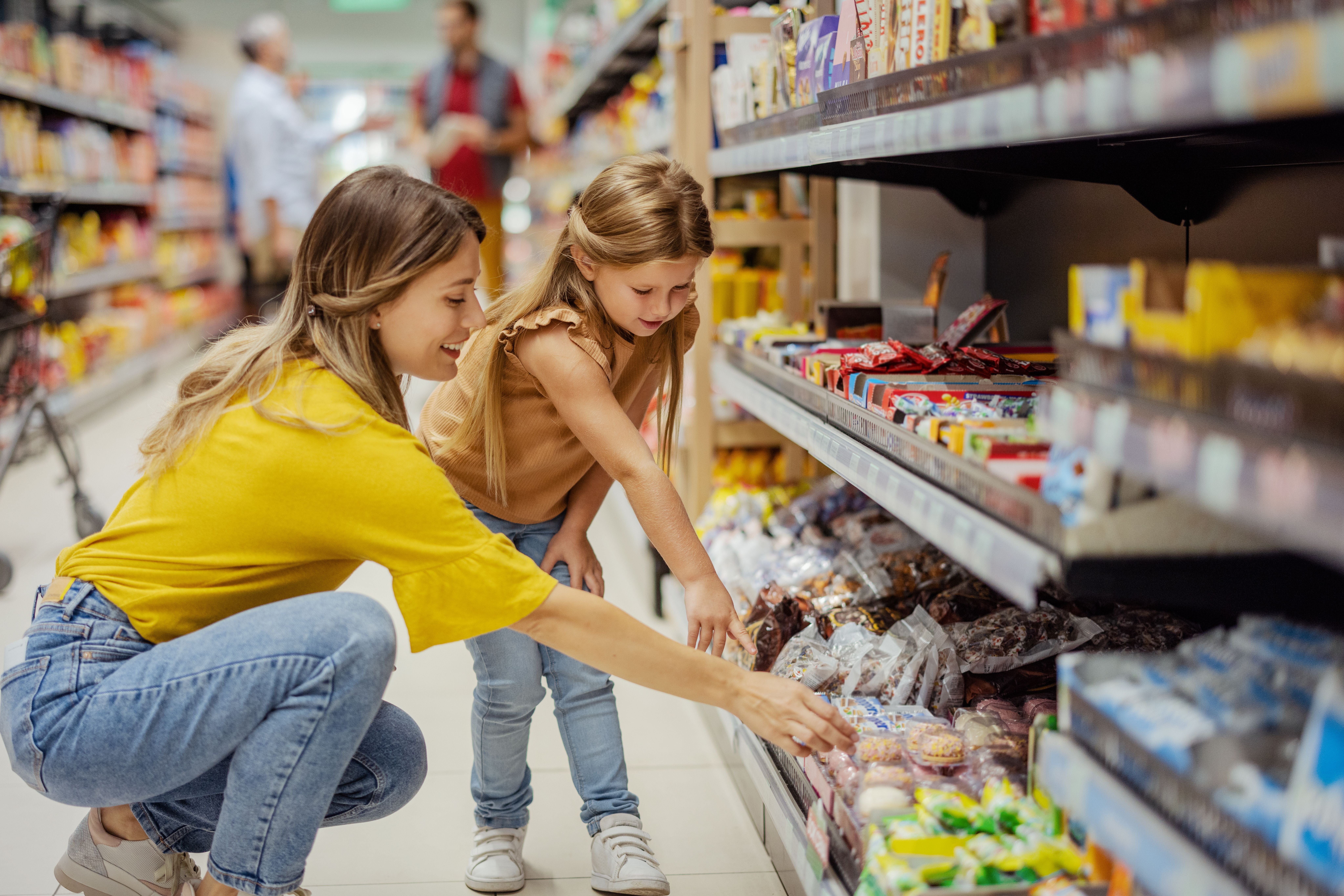 Frau und Mädchen suchen gemeinsam Süßigkeiten im Supermarktregal aus.