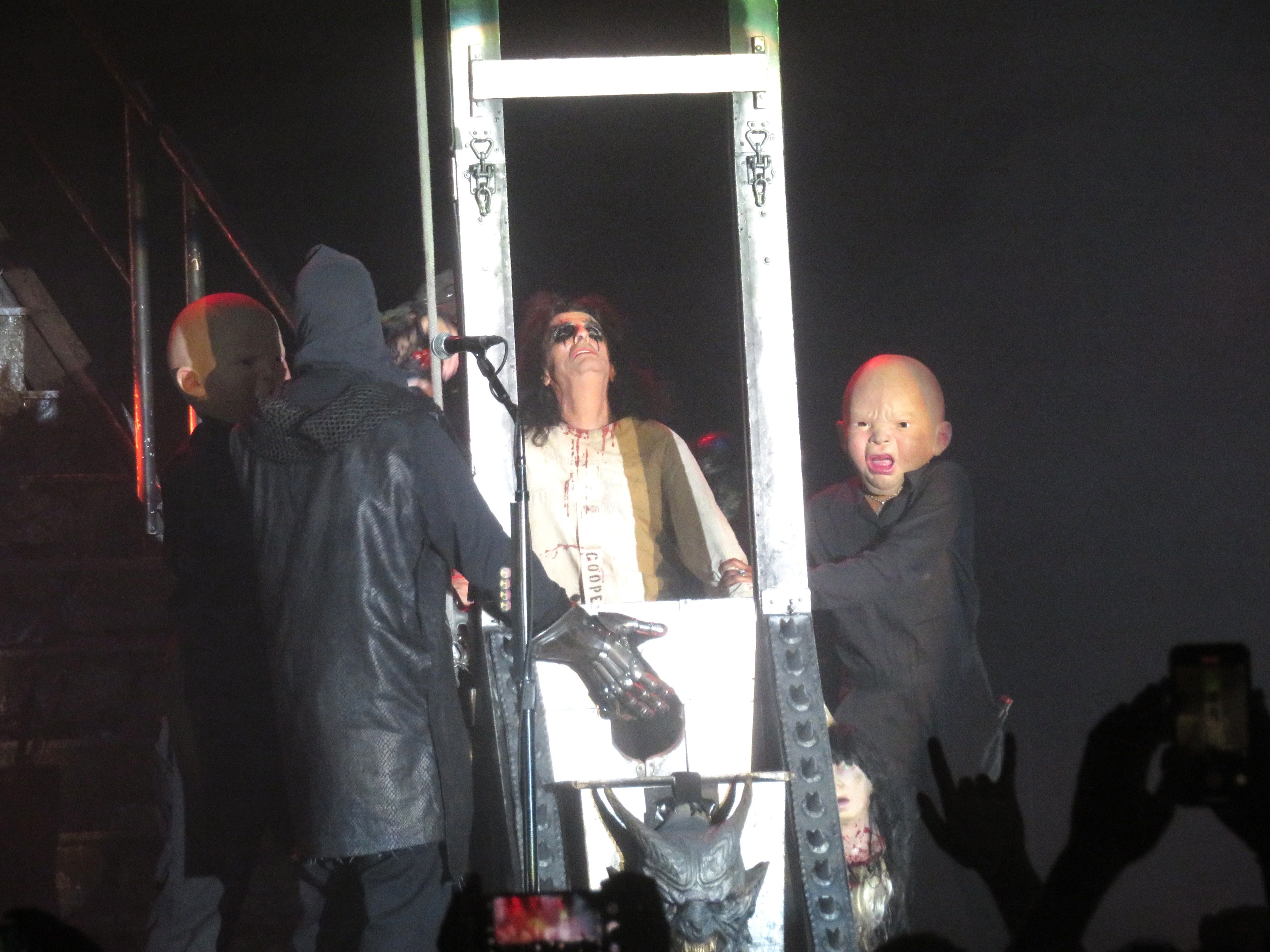 Alice Cooper in einer Guillotine-Szene auf der Bühne mit maskierten Darstellern.