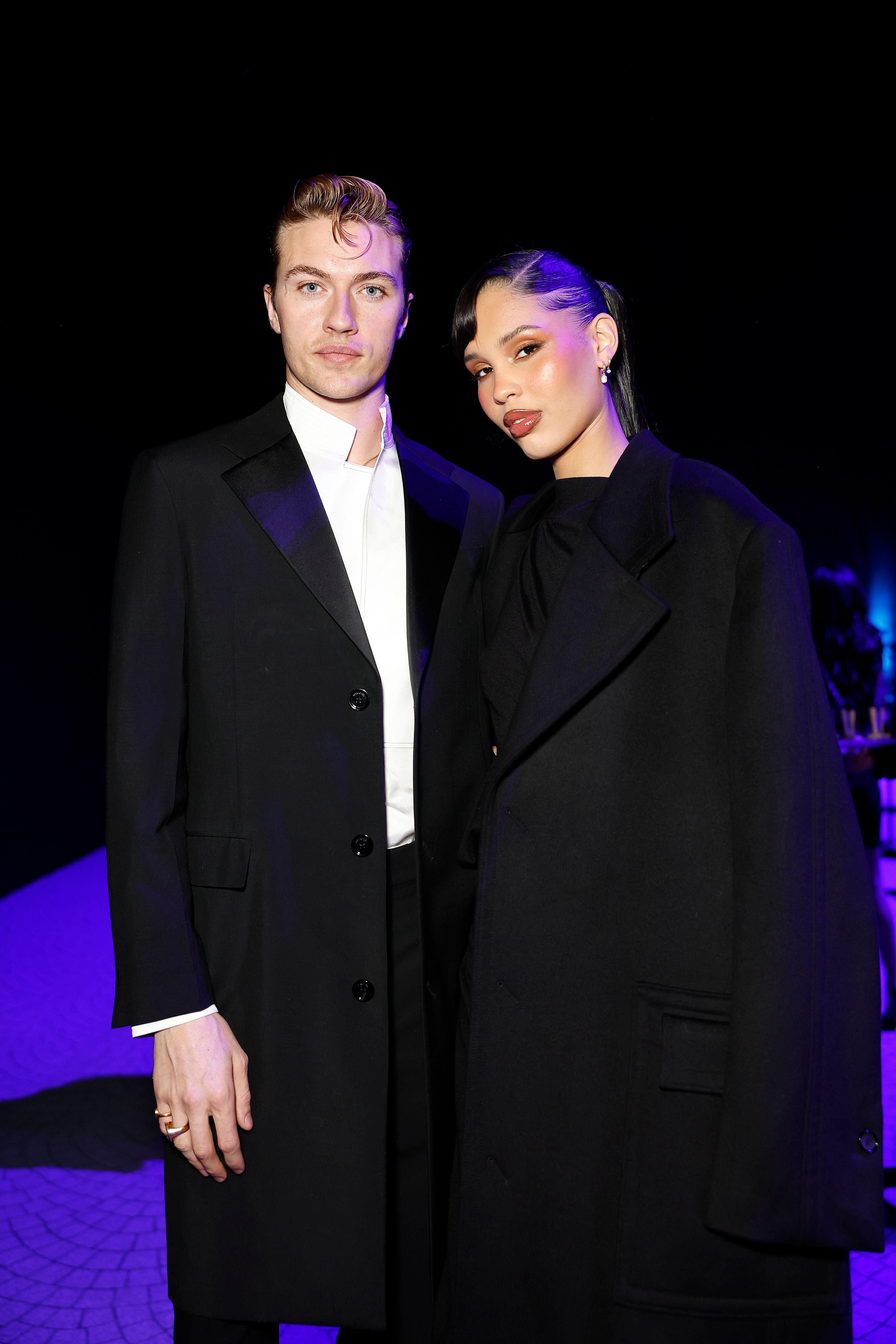 Ein Mann und eine Frau posieren elegant gekleidet auf einem Event vor schwarzem Hintergrund.