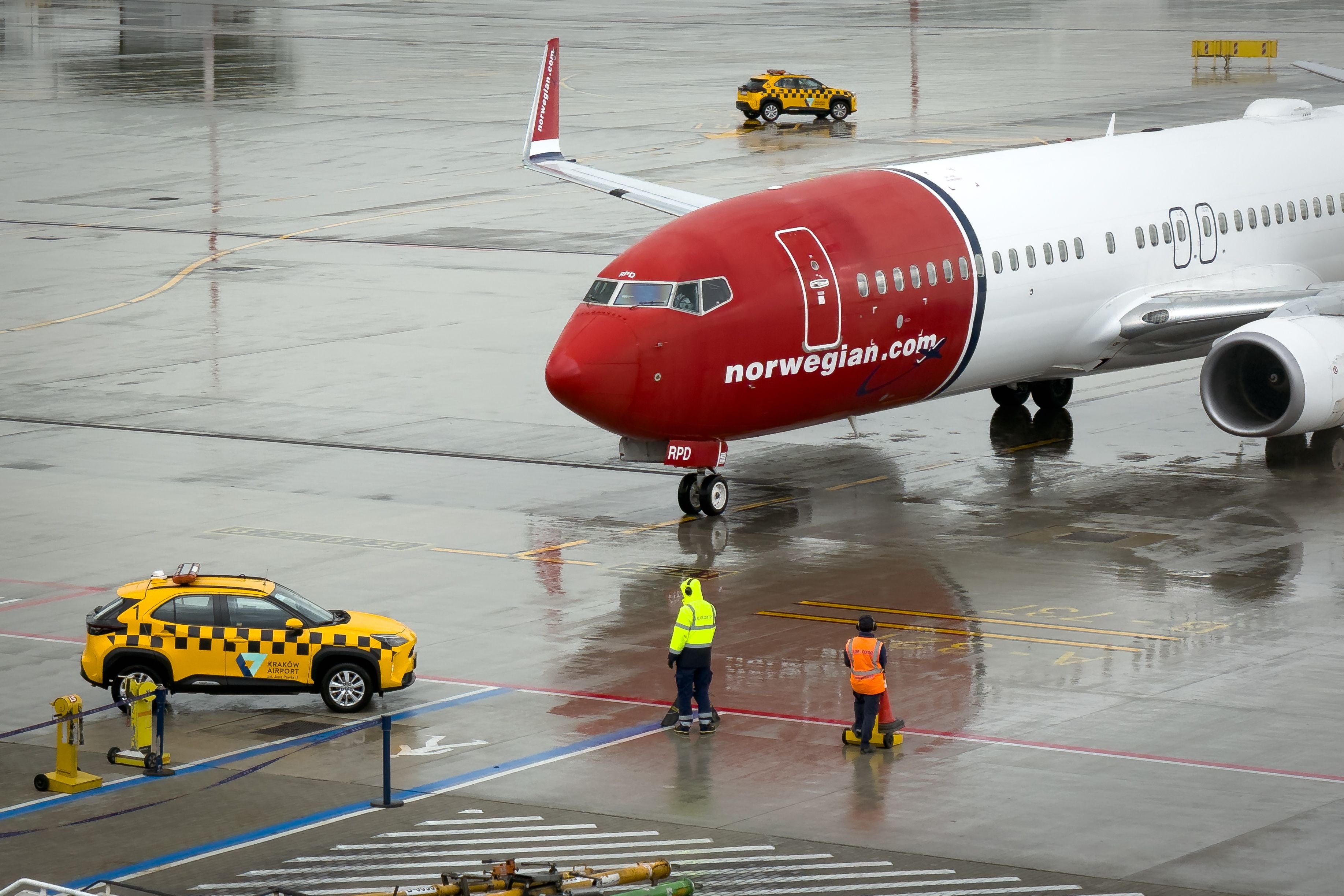 Ein Norwegian-Flugzeug rollt am regnerischen Flughafen Krakau zu bodendienstlichem Personal und gelbem Fahrzeug.