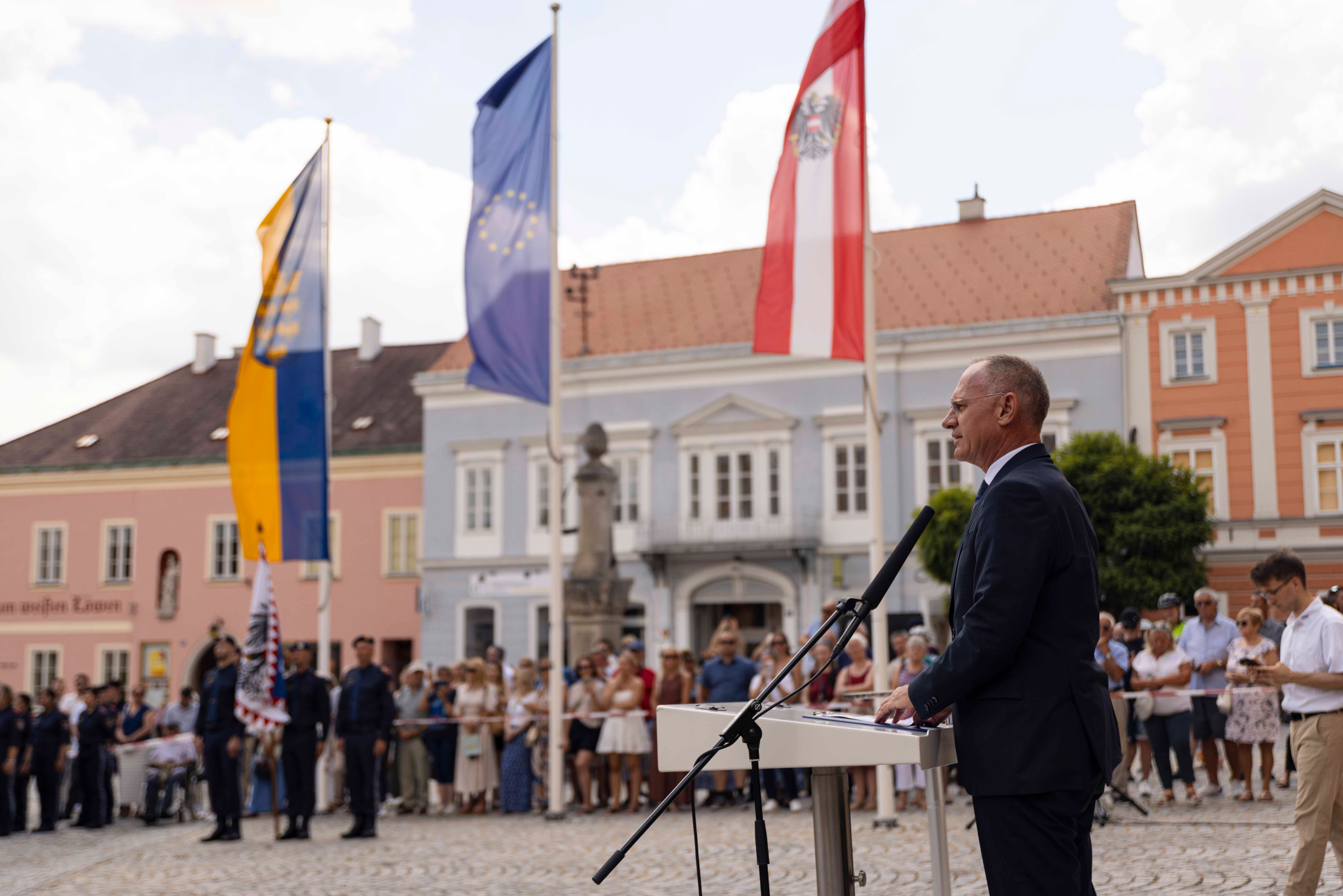 Innenminister Karner spricht bei einer Außenveranstaltung mit Publikum und Fahnen im Hintergrund.