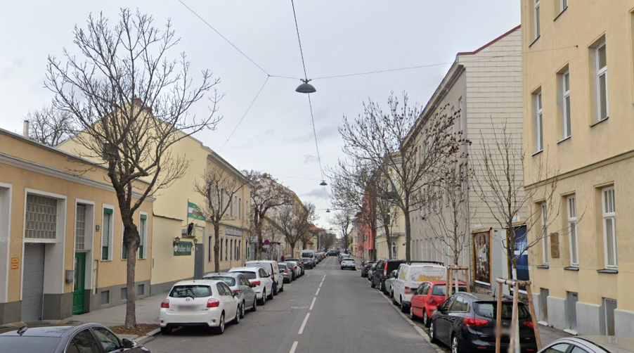 Schmale Wohnstraße mit parkenden Autos, kahlen Bäumen und beidseitigen Gehwegen.