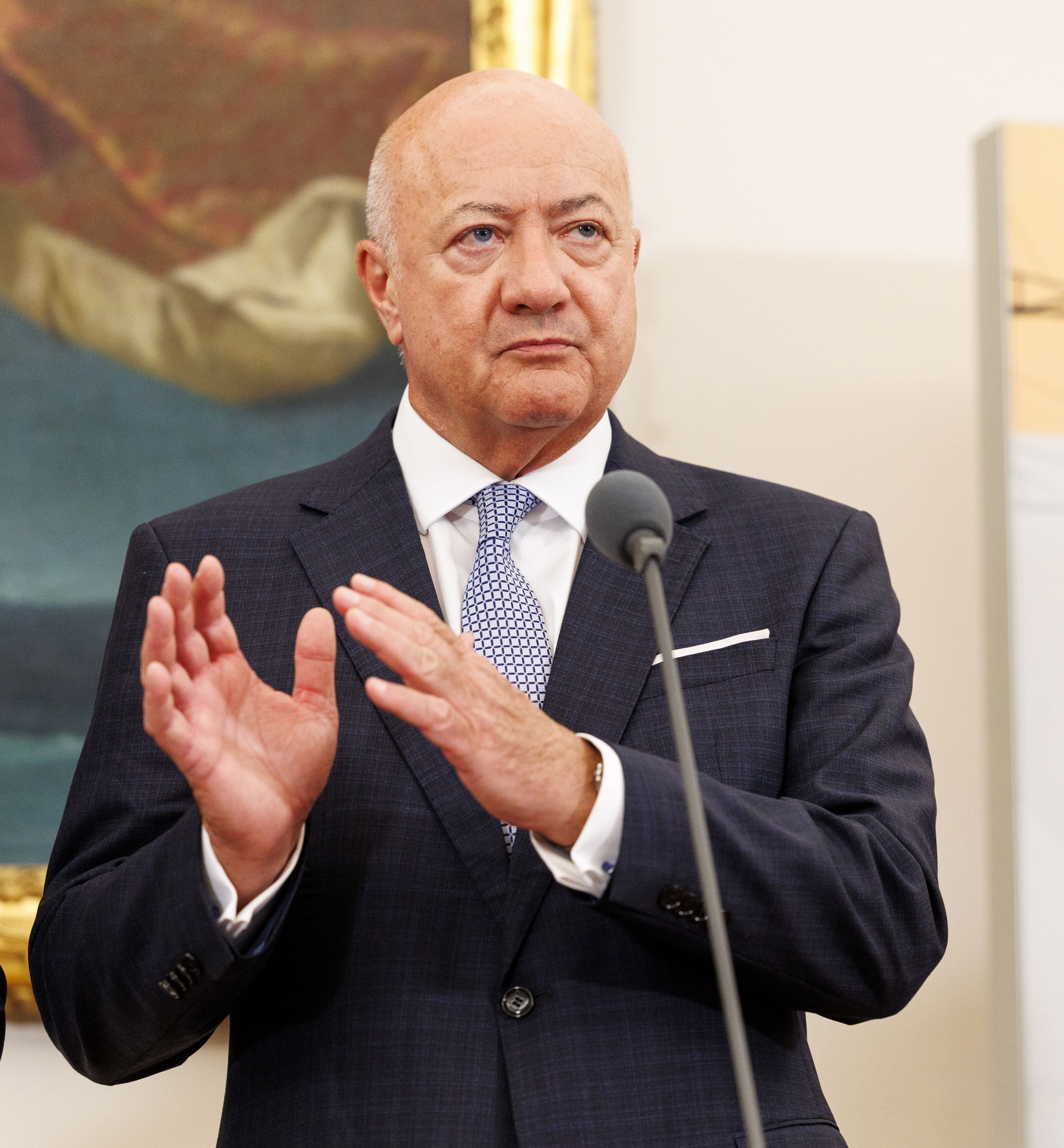 Ein Mann im Anzug steht an einem Mikrofon und spricht bei einer Pressekonferenz.