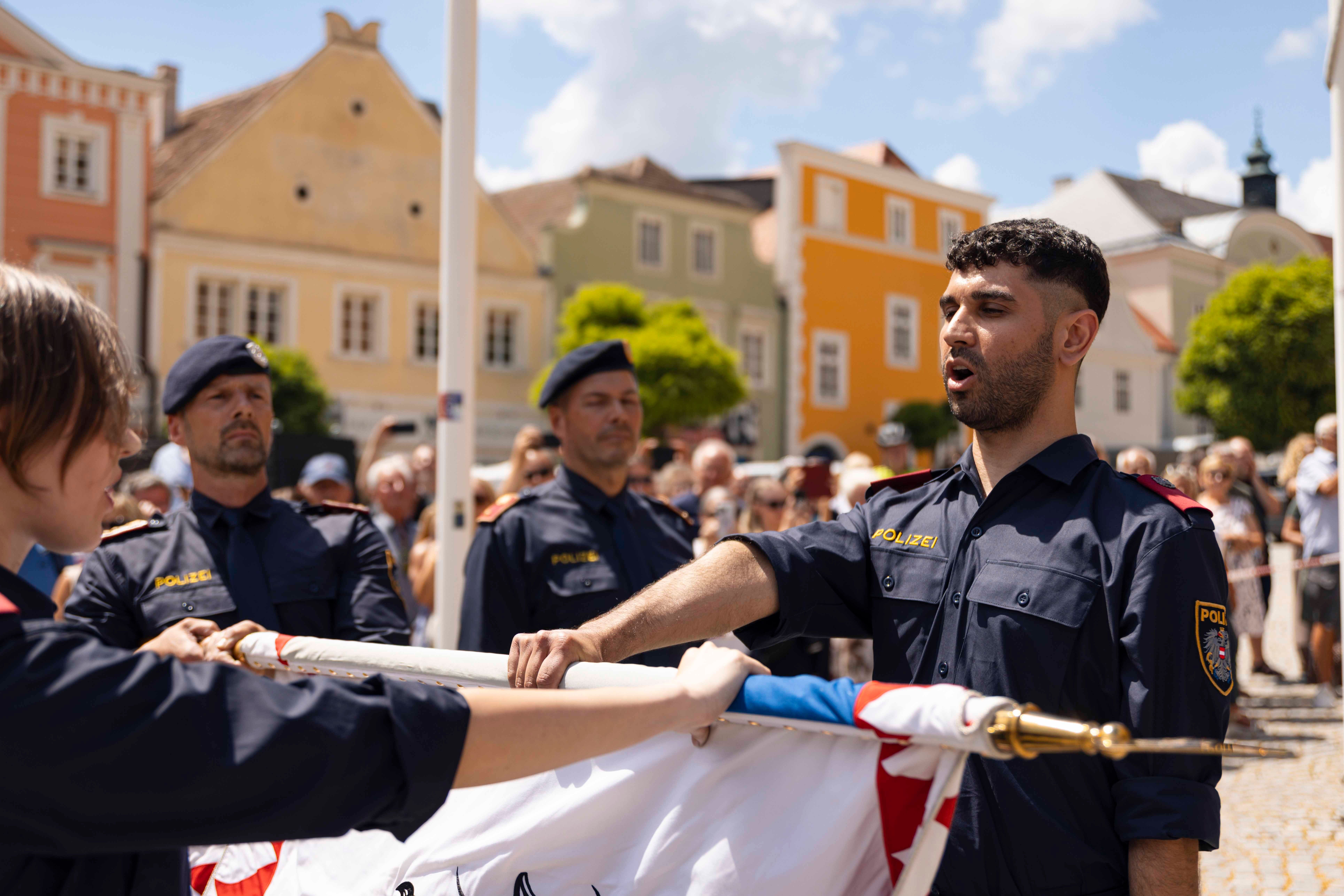 Polizisten legen im Freien einen Eid auf die Fahne ab, Zuschauer im Hintergrund.
