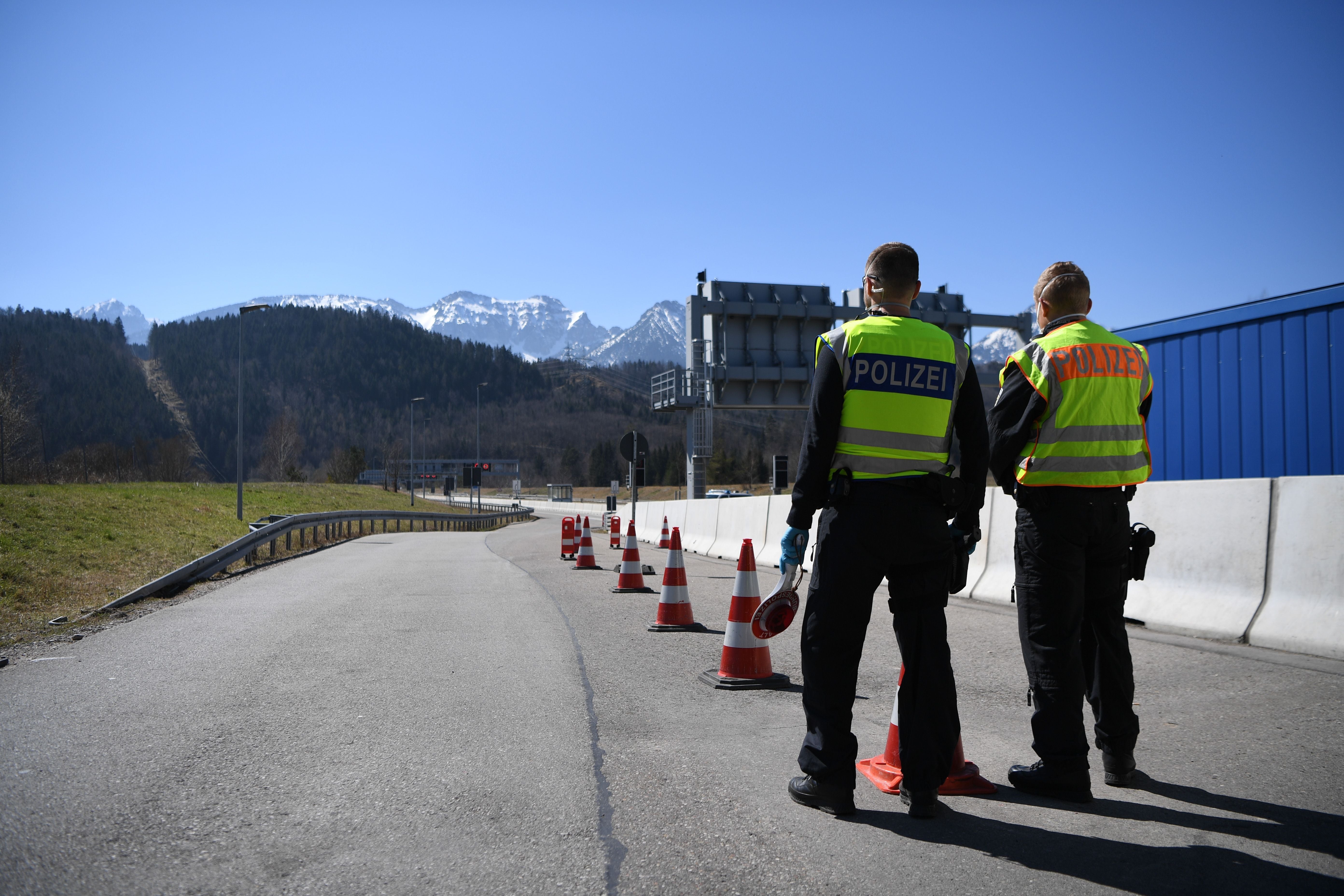 Zwei Polizisten stehen an einem Straßensperrpunkt mit Verkehrshütchen vor Bergkulisse.