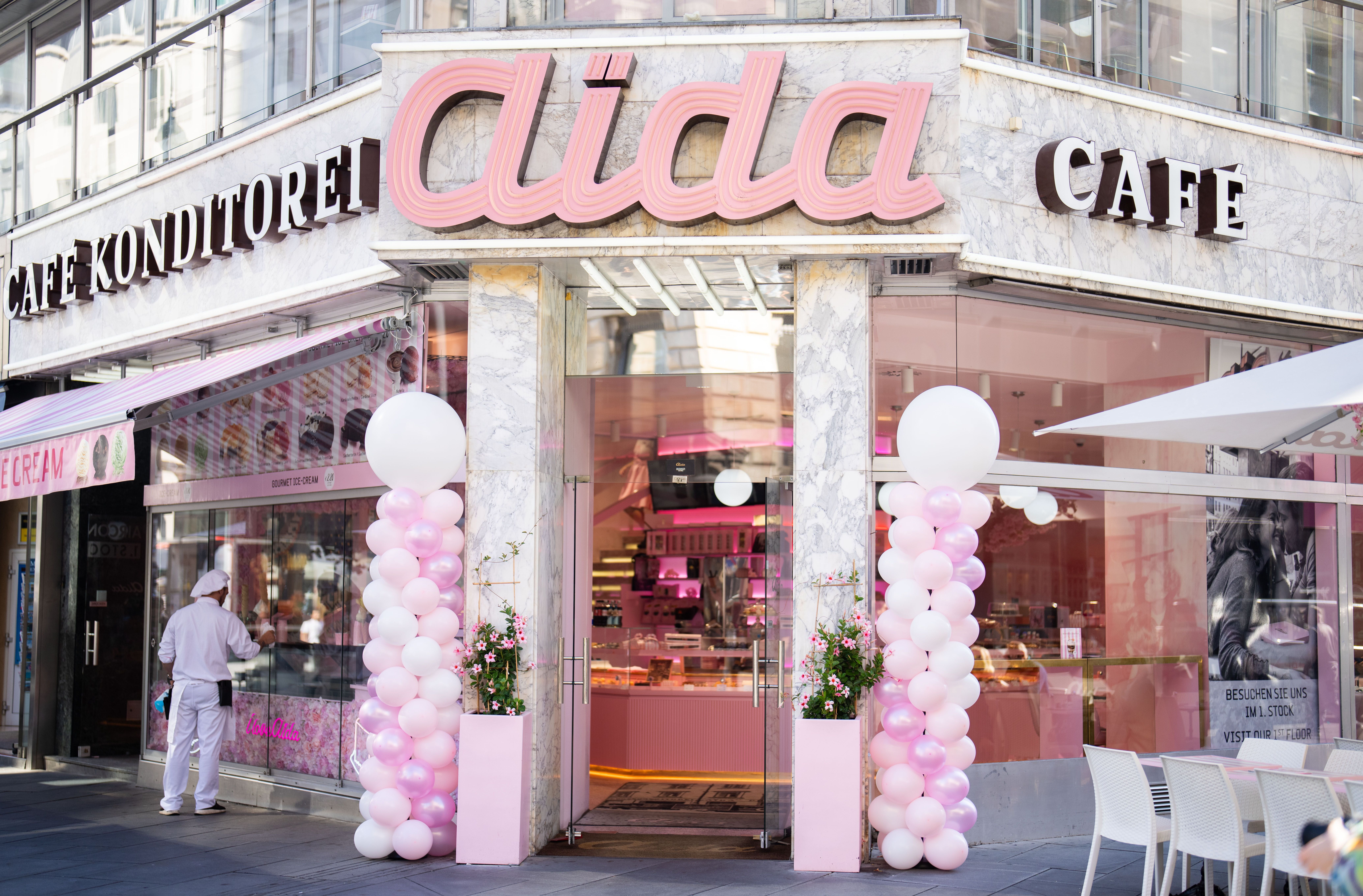 Außenansicht eines Aida-Cafés mit rosa und weißen Luftballons am Eingang in Wien.