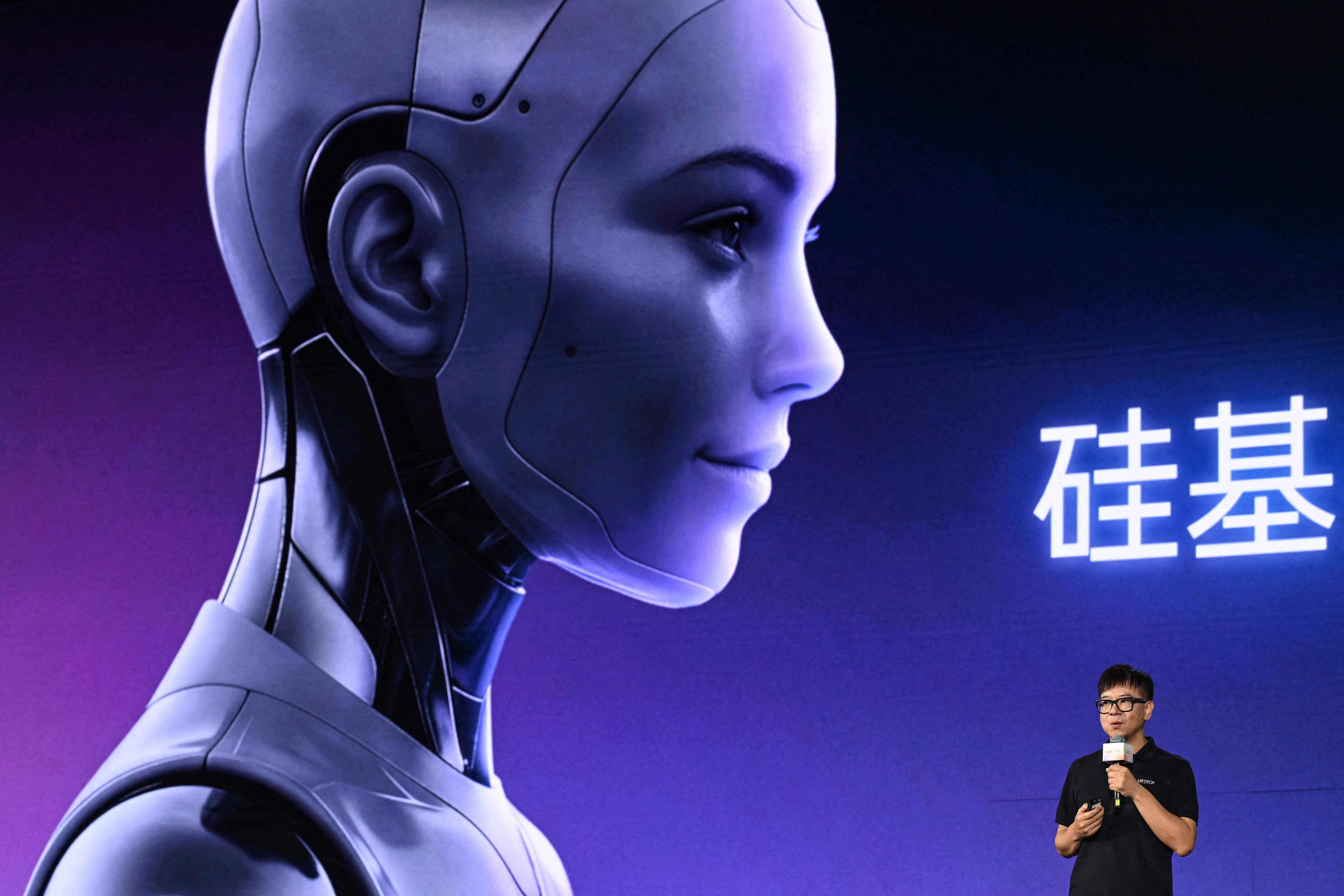 Ein Mann präsentiert auf einer Bühne vor einem großen Bild eines humanoiden Roboters mit menschlichem Gesicht.