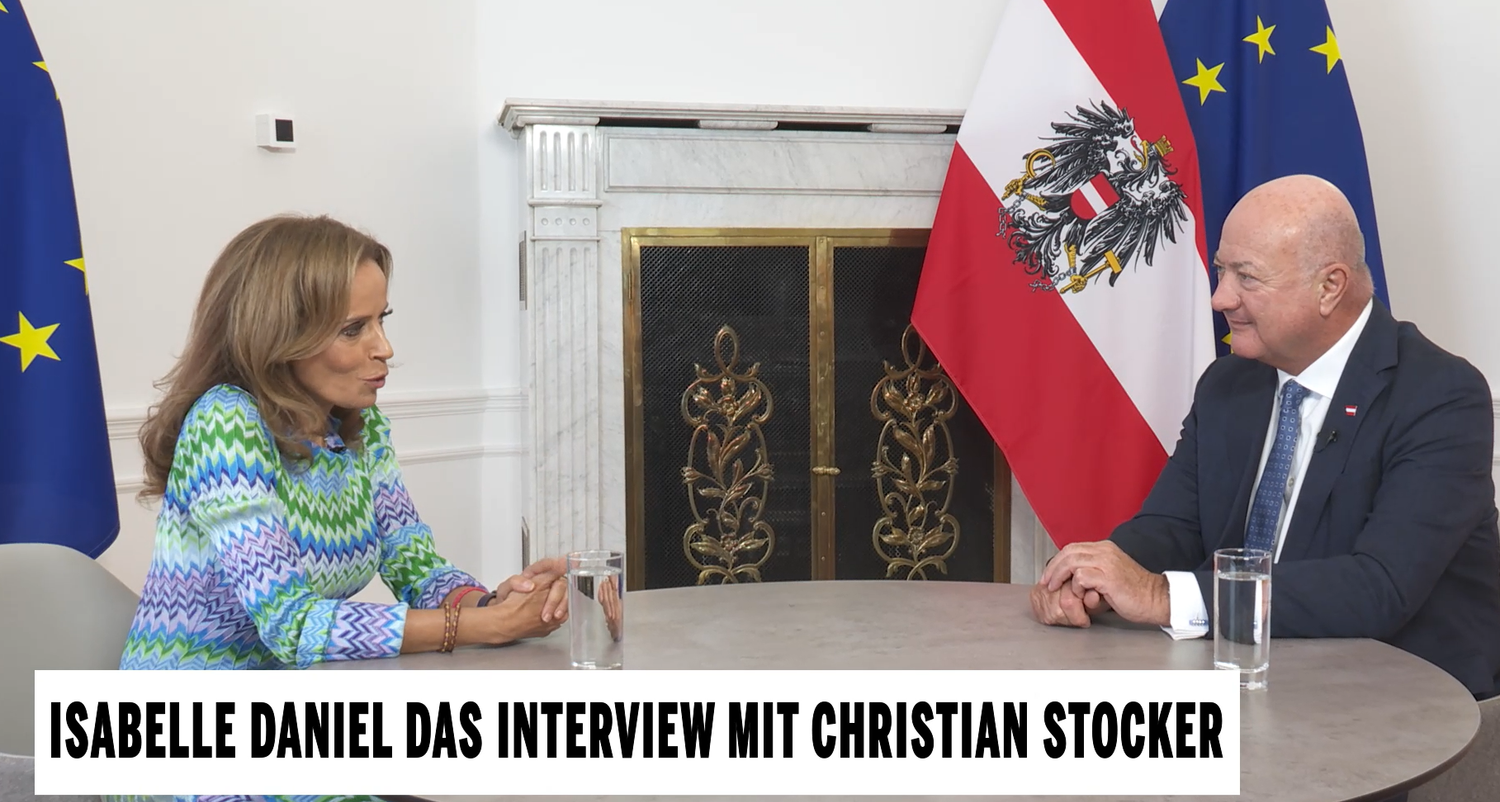 Isabelle Daniel interviewt Christian Stocker an einem Tisch mit österreichischer Flagge im Hintergrund.