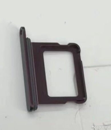 Burgunderrotes SIM-Kartenfach für ein iPhone 18 Pro auf weißer Oberfläche. Offenbar schlecht beleuchtet.