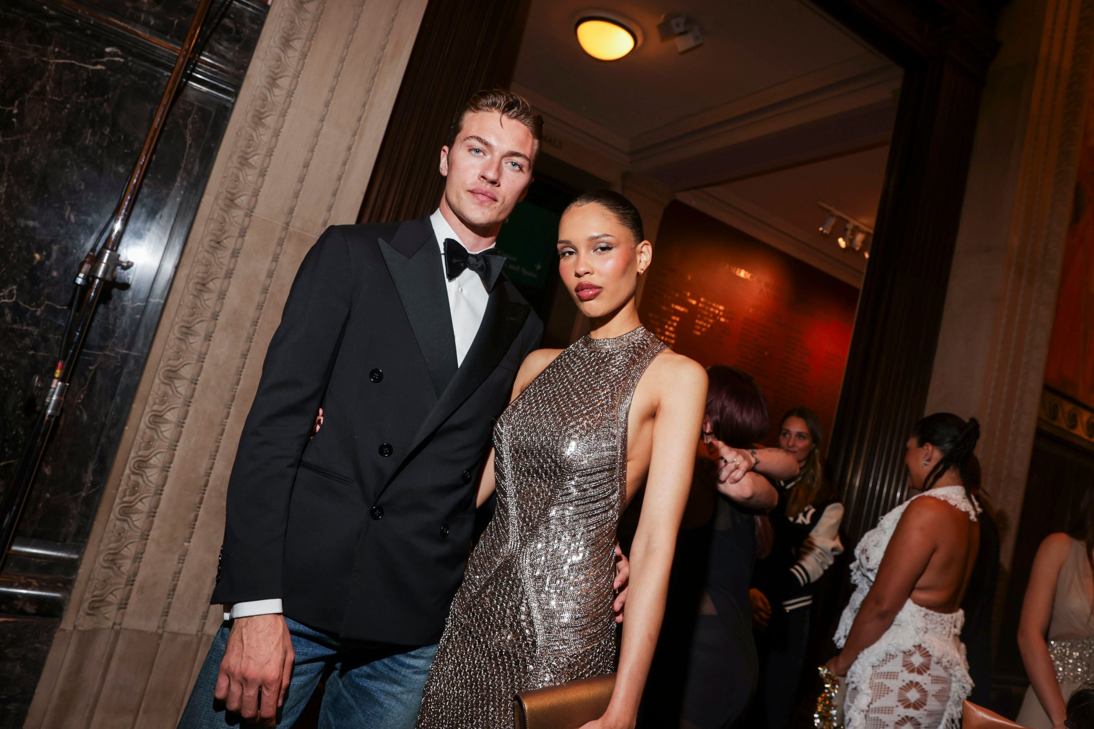 Ein Mann im Smoking und eine Frau im funkelnden Kleid posieren elegant bei einer Abendveranstaltung.