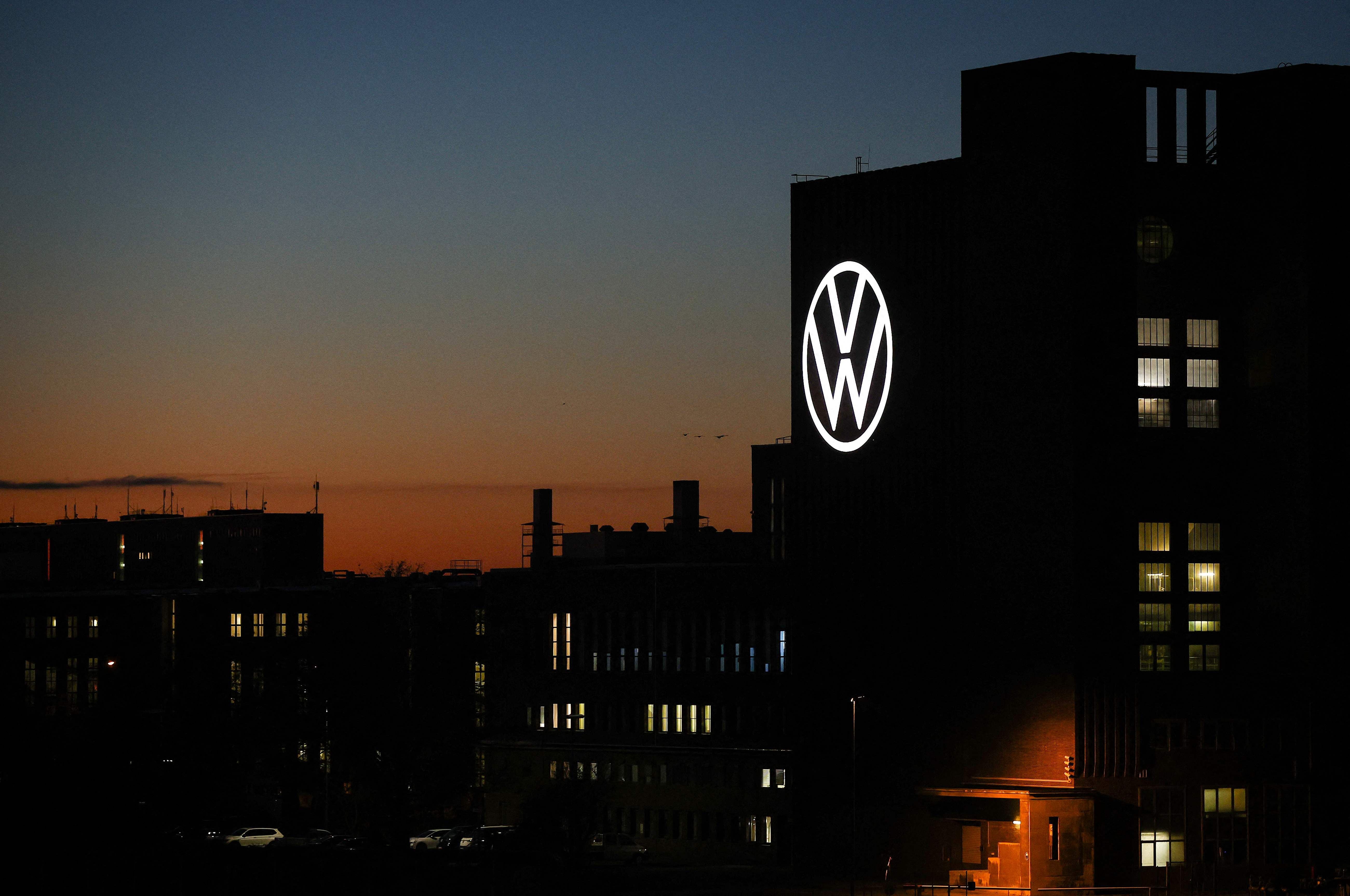 Beleuchtetes VW-Logo am Kraftwerksgebäude in Wolfsburg bei Sonnenuntergang.