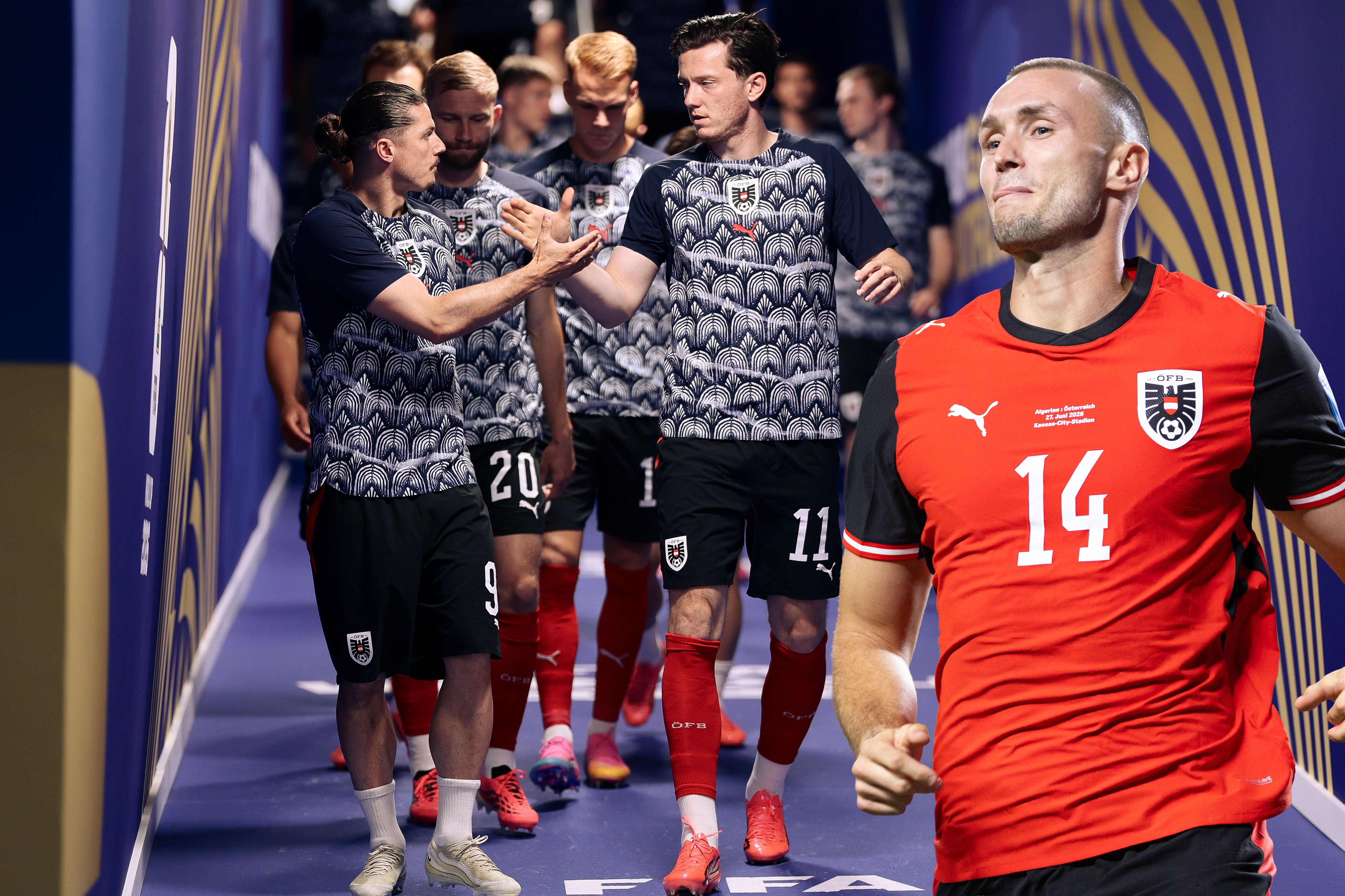 Österreichische Fußballspieler im Gang, einer im roten Trikot im Vordergrund, andere jubeln im Hintergrund.