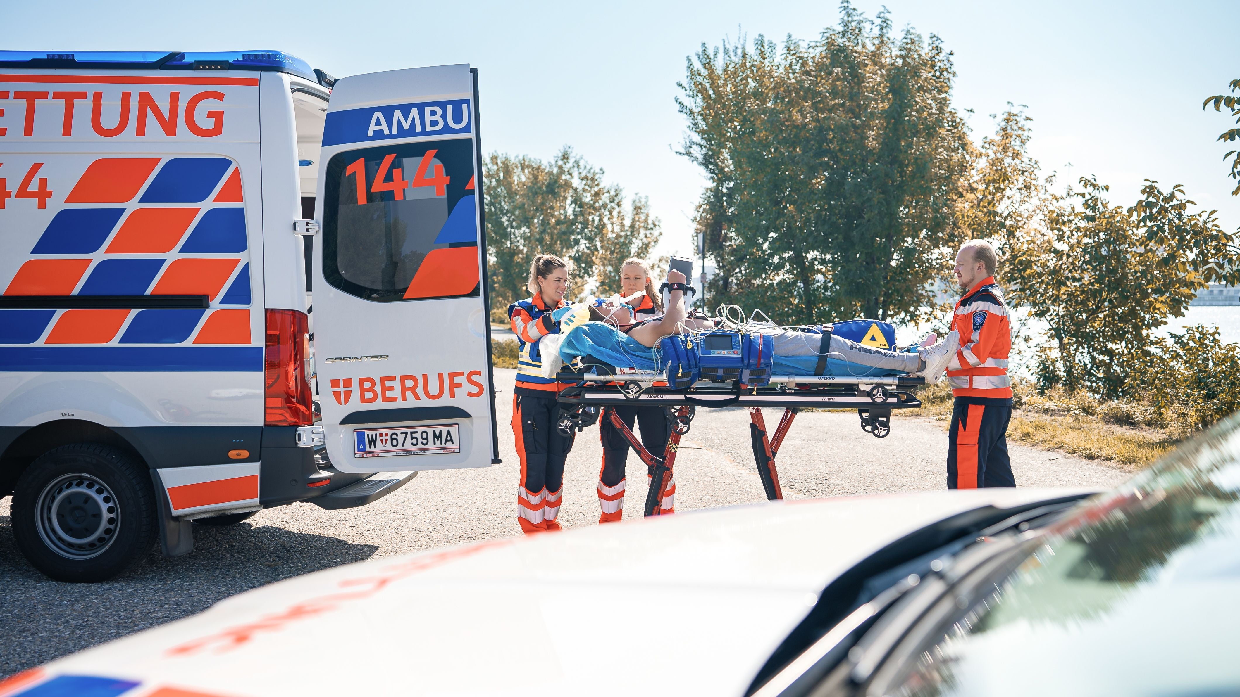 Sanitäter verladen einen Patienten auf einer Trage in einen Rettungswagen bei Tageslicht.