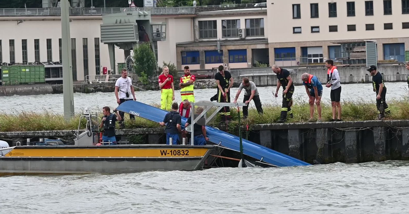 Rettungskräfte und Helfer bergen ein gekentertes Ruderboot aus dem Wasser am Flussufer.