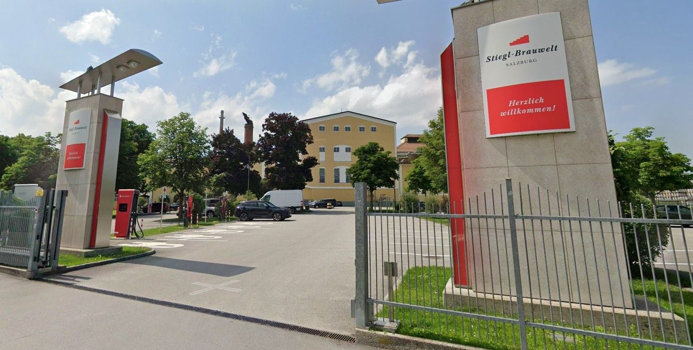 Eingang zur Stiegl-Brauwelt Salzburg mit Willkommensschild und Parkplatz.