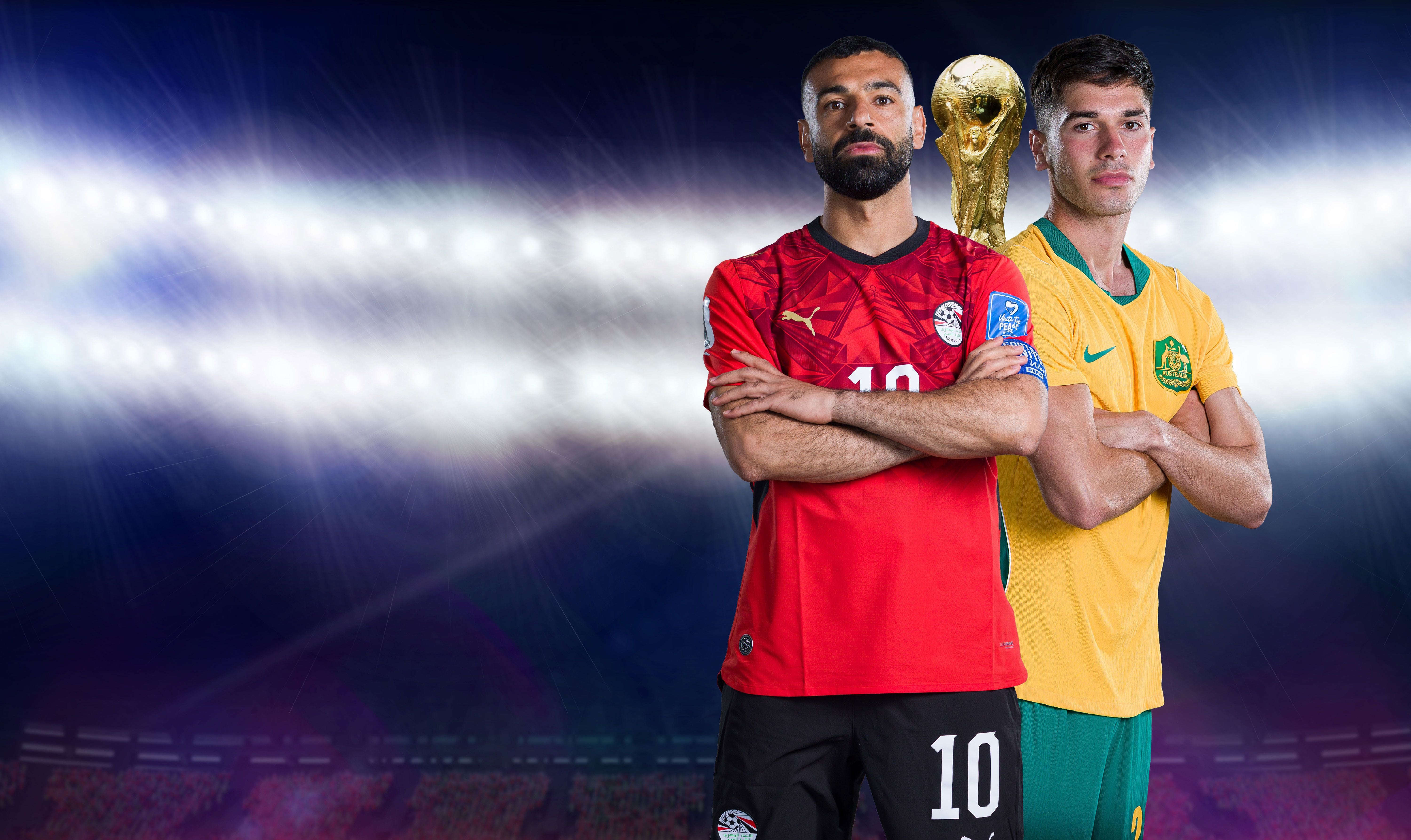 Zwei Fußballspieler aus Ägypten und Australien stehen mit verschränkten Armen vor einem Pokal im Stadion.