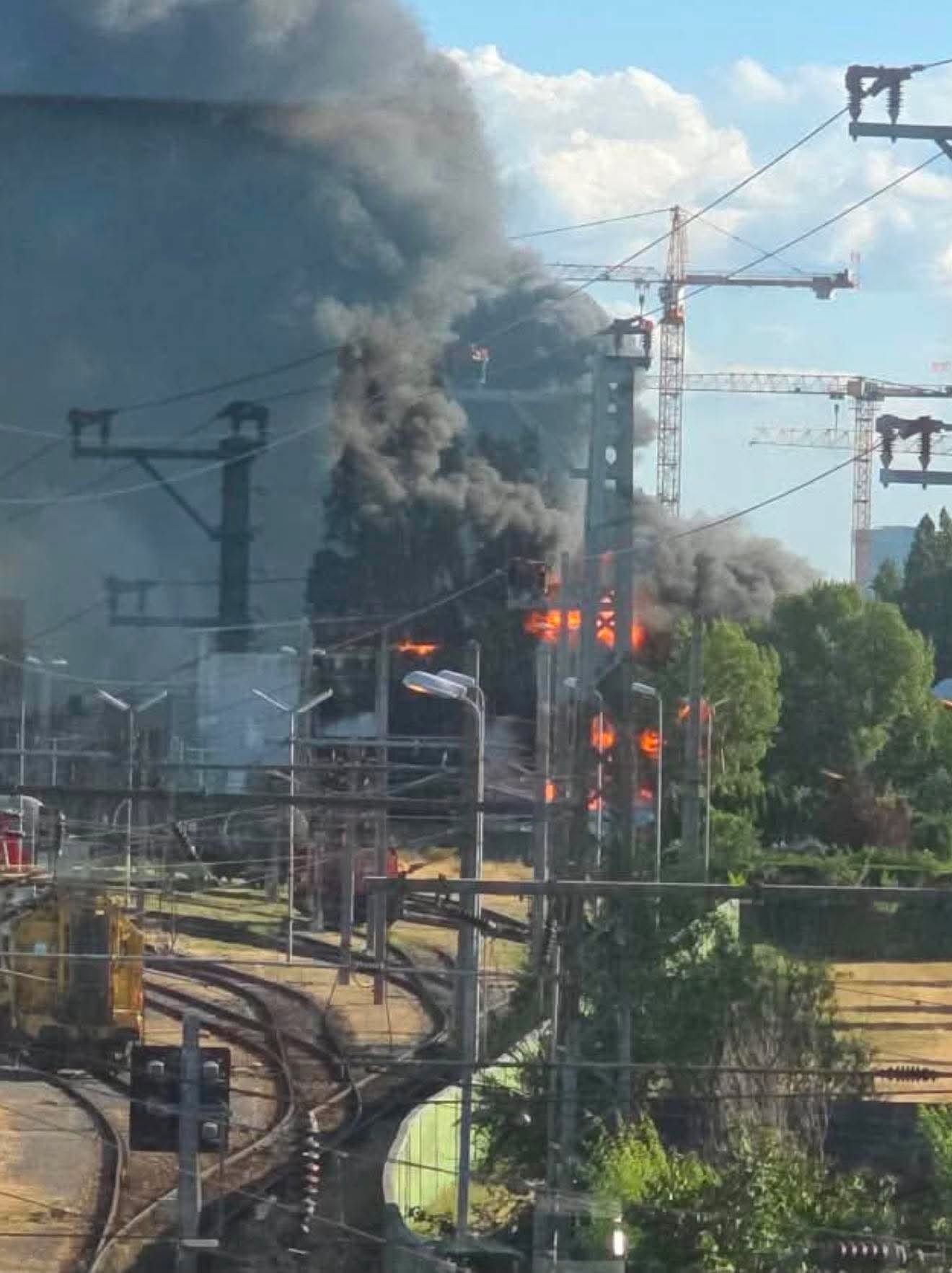 Dichter Rauch und Flammen an Bahngleisen im Bereich eines Bahnhofs, im Hintergrund Baukräne.