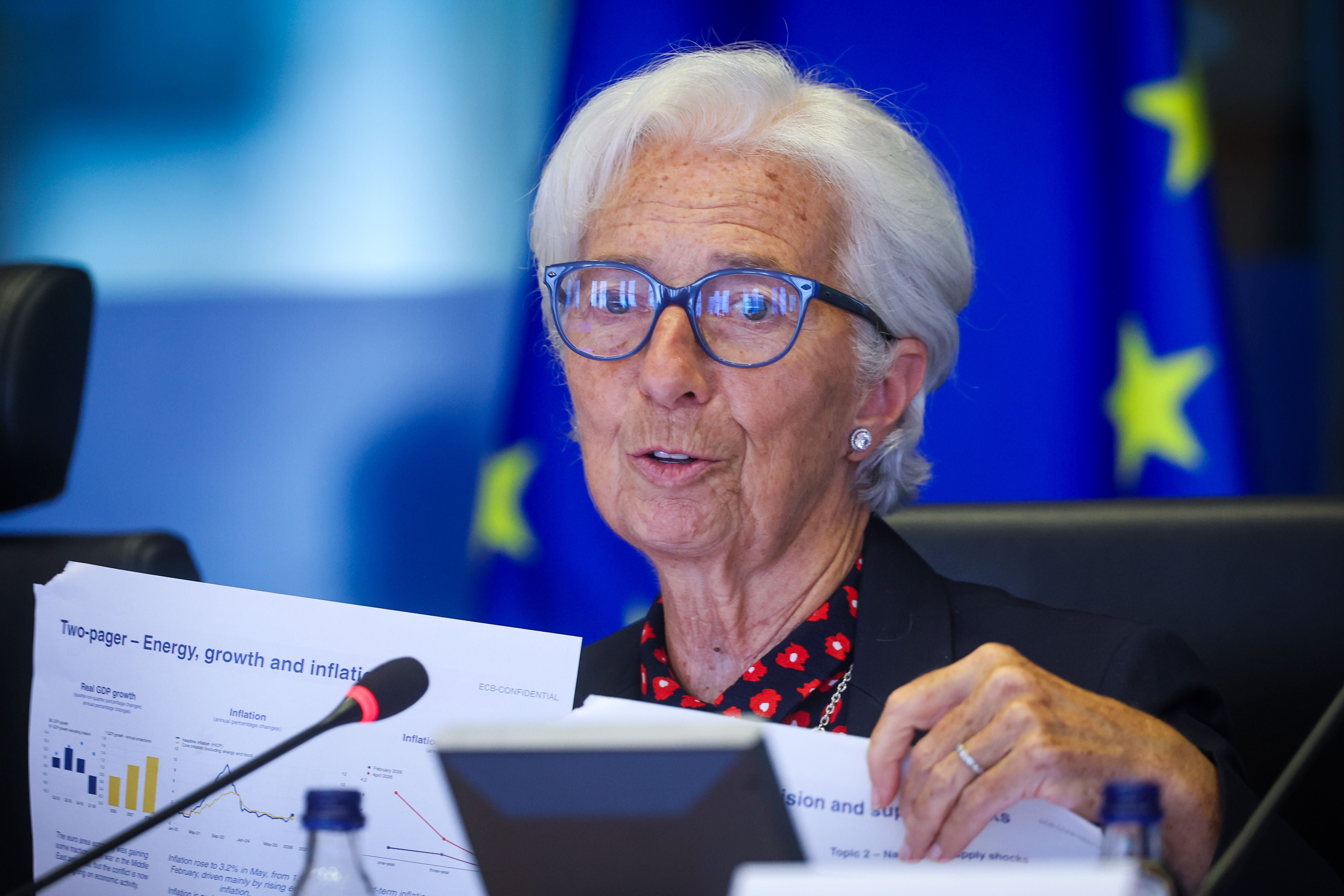 Eine ältere Frau mit weißen Haaren spricht in einem Konferenzraum und hält Diagramme in den Händen.