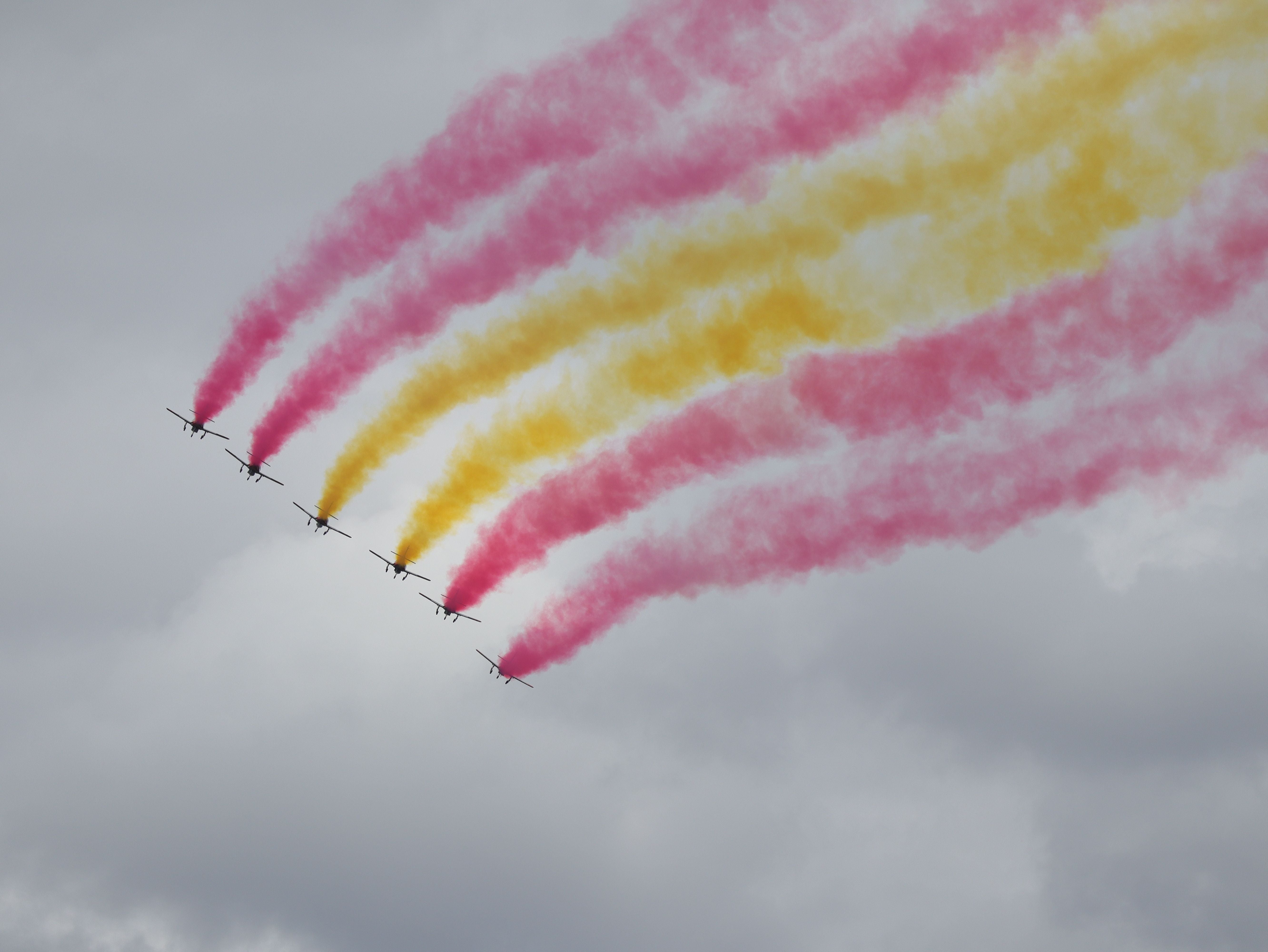 Sechs Flugzeuge ziehen rote und gelbe Rauchstreifen am grauen Himmel bei einer Flugshow.