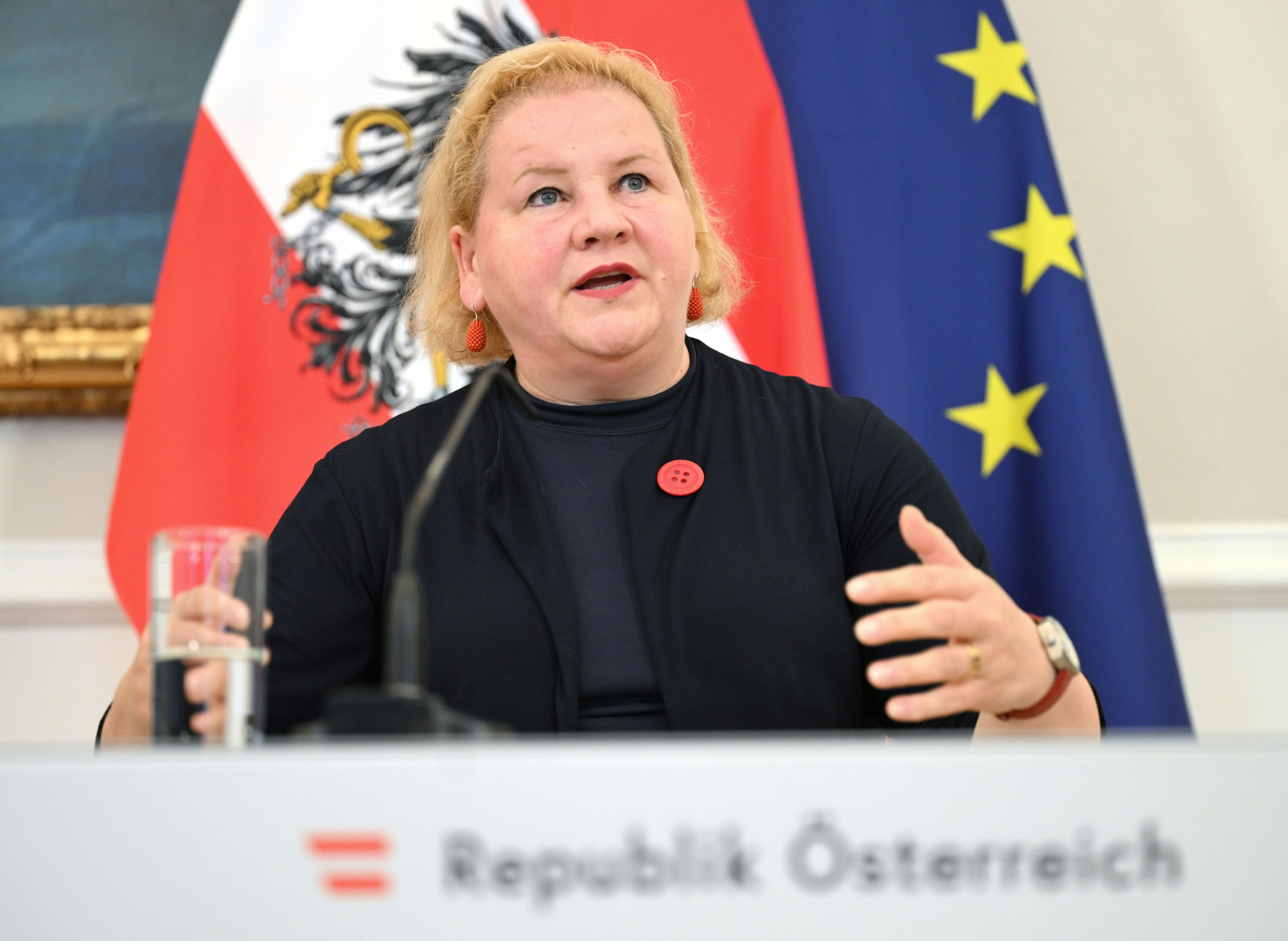 Eine Frau spricht bei einer Pressekonferenz vor österreichischer und EU-Flagge.