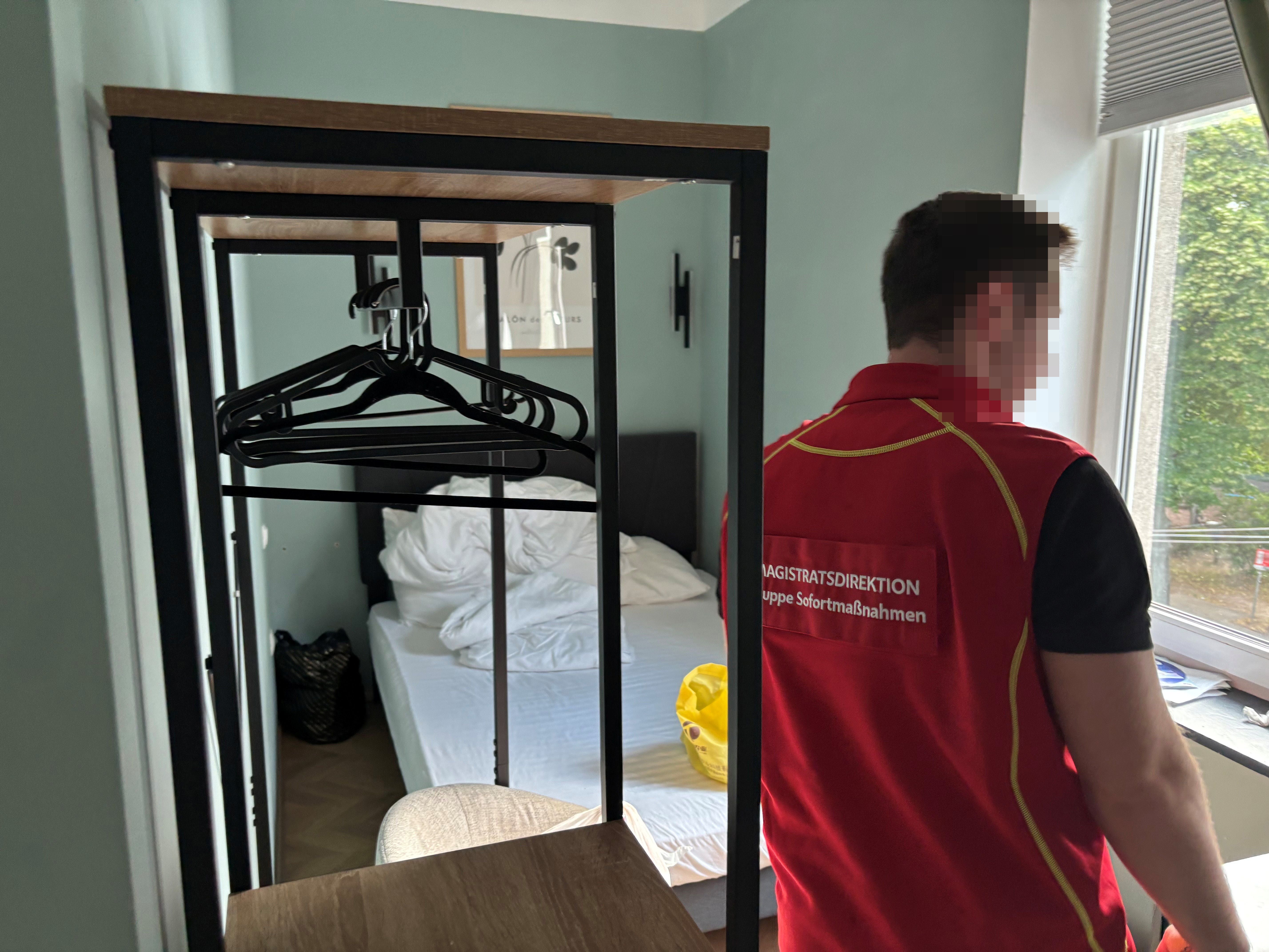 Ein Mann mit roter Weste steht in einem Hotelzimmer und blickt aus dem Fenster.