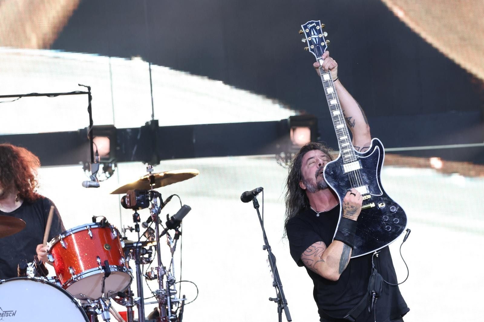 Gitarrist der Foo Fighters hebt seine E-Gitarre auf einer Konzertbühne in die Luft.
