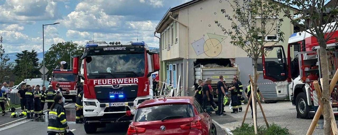 Mehrere Feuerwehrfahrzeuge und Einsatzkräfte vor einem beschädigten Haus mit Loch in der Wand.