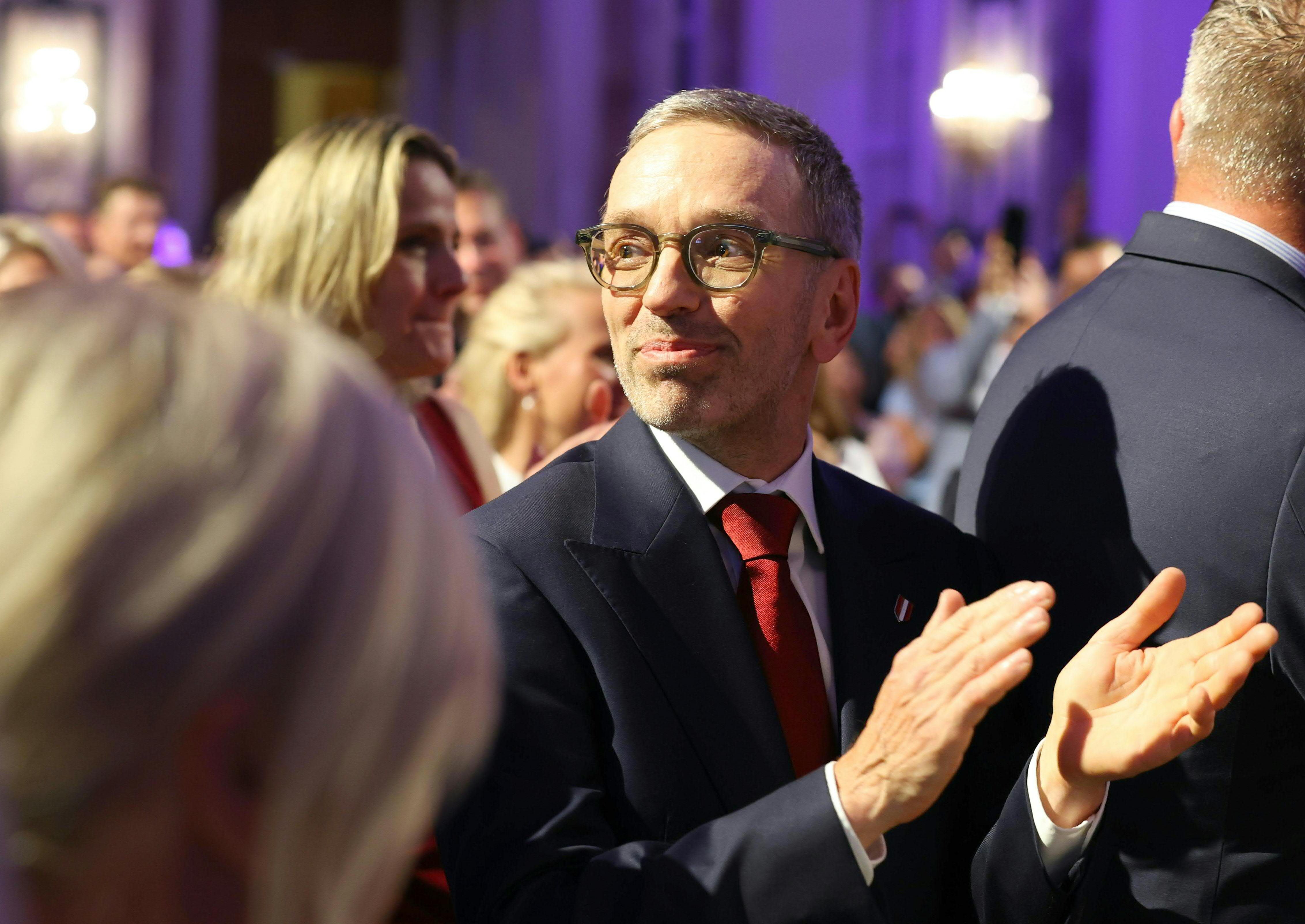 Ein Mann im Anzug applaudiert bei einer Feier in einem festlich beleuchteten Saal.