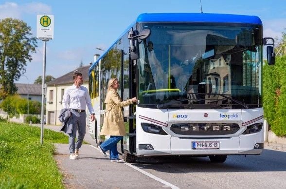 Zwei Personen steigen an einer Bushaltestelle in Niederösterreich in einen Linienbus ein.
