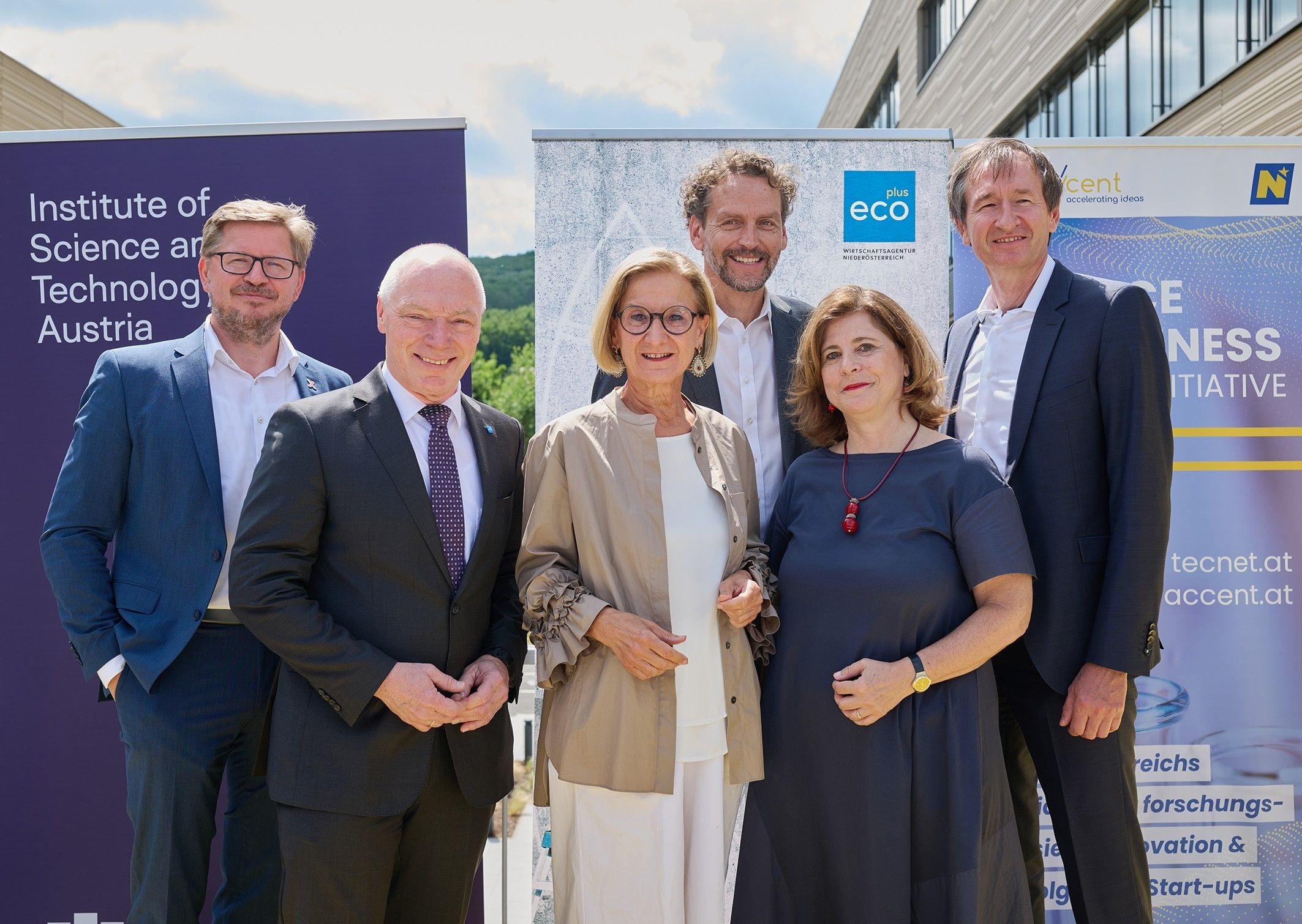 Sechs Personen posieren gemeinsam vor Werbetafeln im Freien für ein Gruppenfoto.