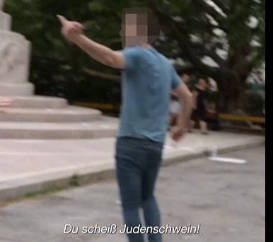 Eine Person steht draußen, zeigt einen beleidigenden Gestus und beleidigt im Untertitel.