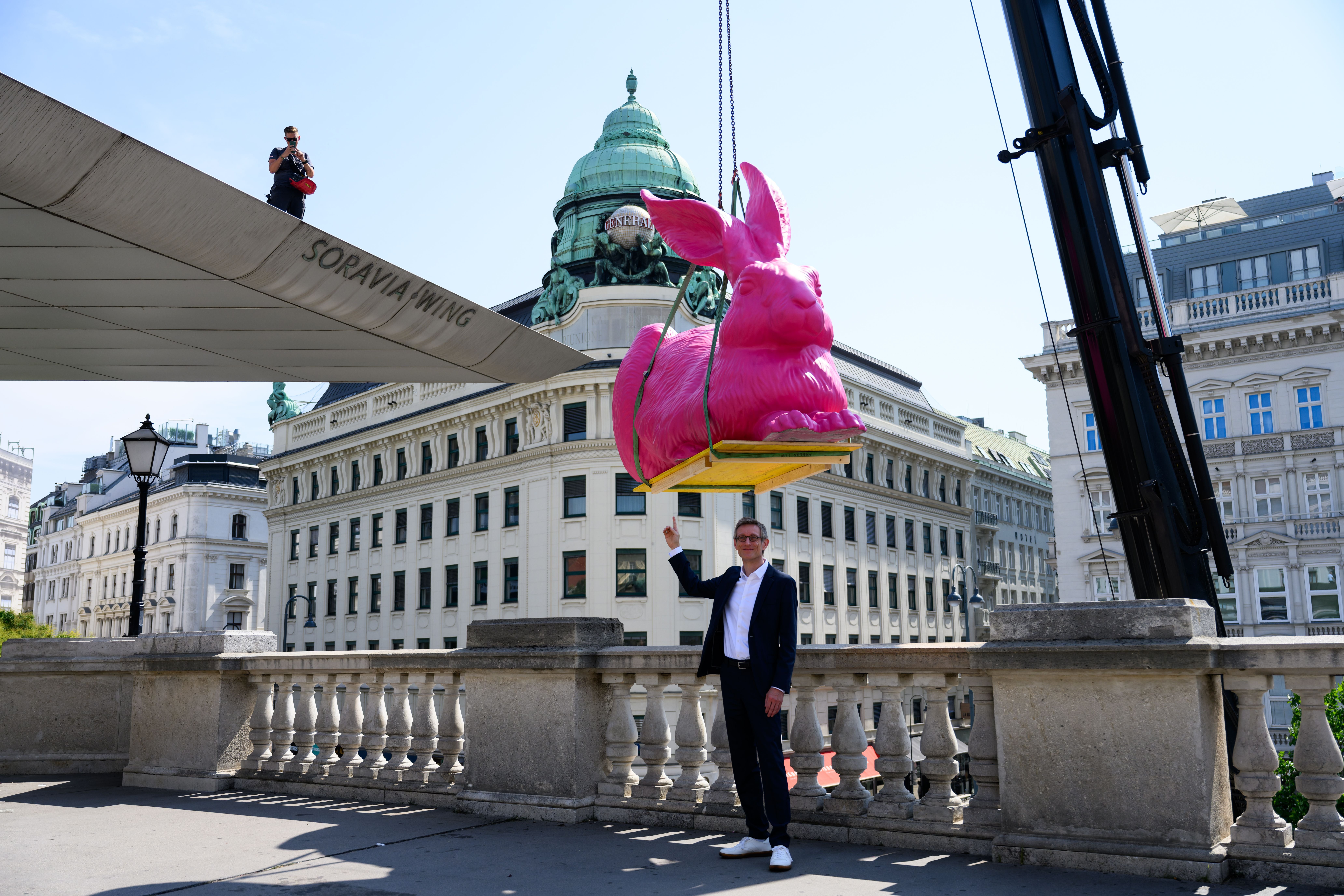 Ein Mann steht unter einer riesigen pinken Hasenskulptur, die per Kran in Wien installiert wird.