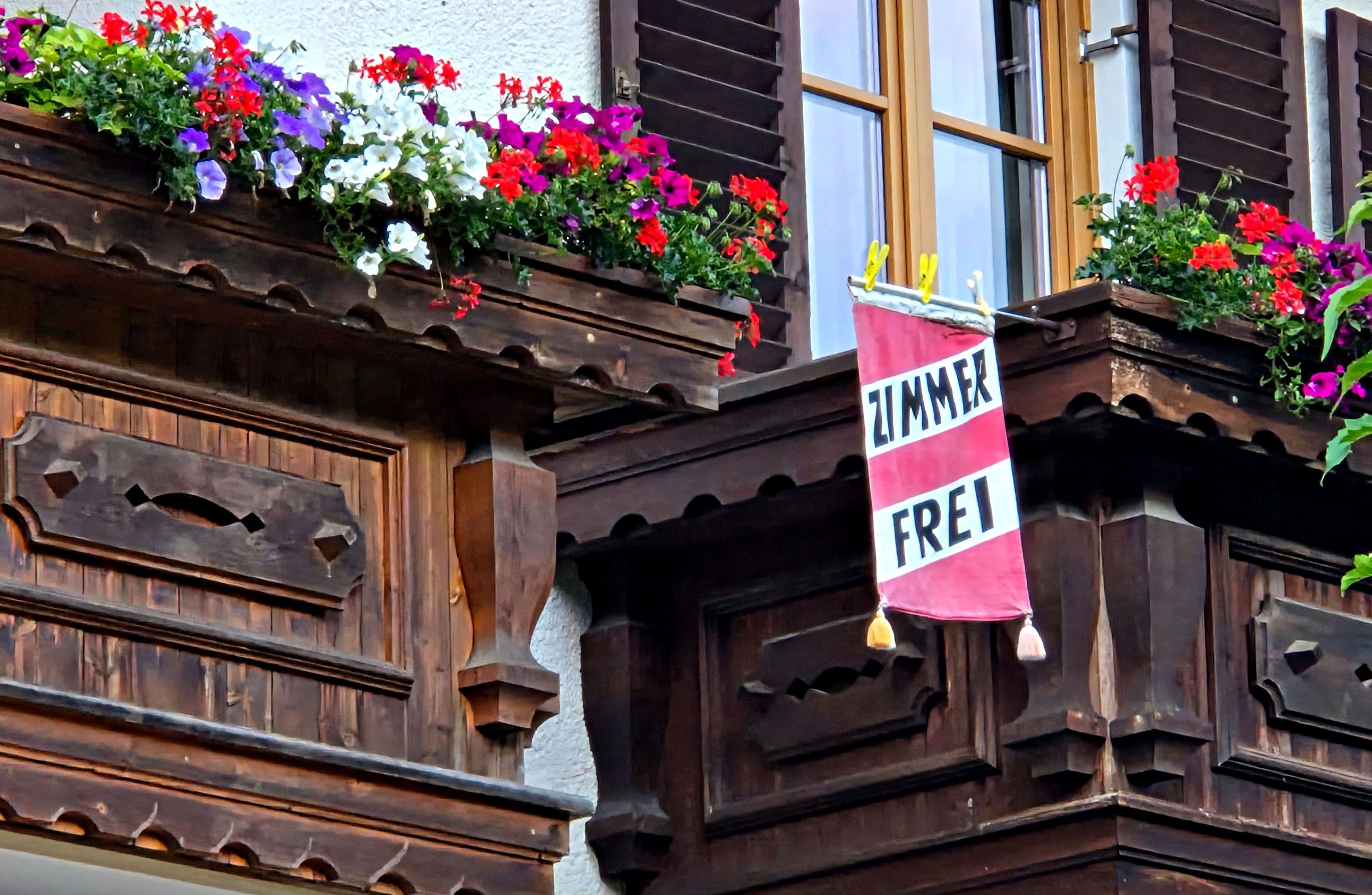 Ein Balkon mit Blumen und einer Fahne "Zimmer frei" an einem Holzhaus in Kals.