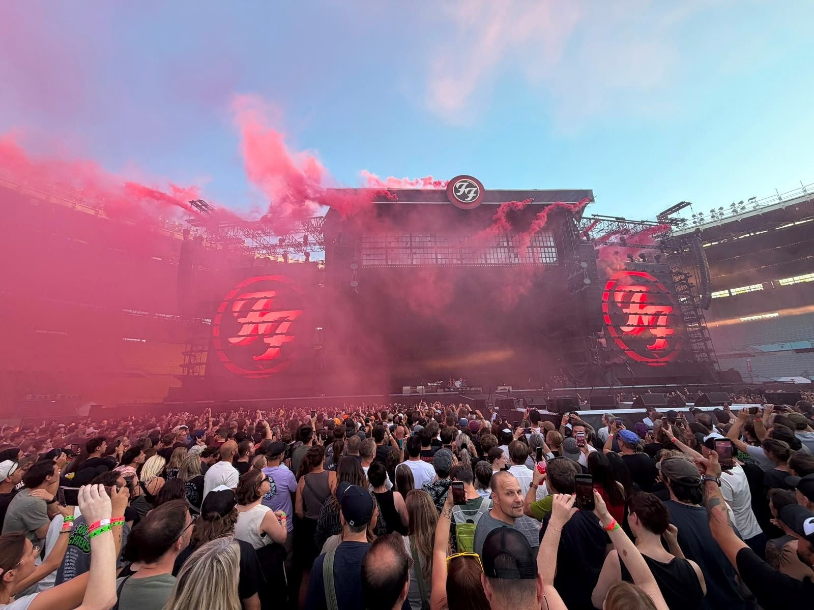 Menschenmenge vor einer Bühne mit rotem Rauch und Foo Fighters-Logo bei einem Konzert.