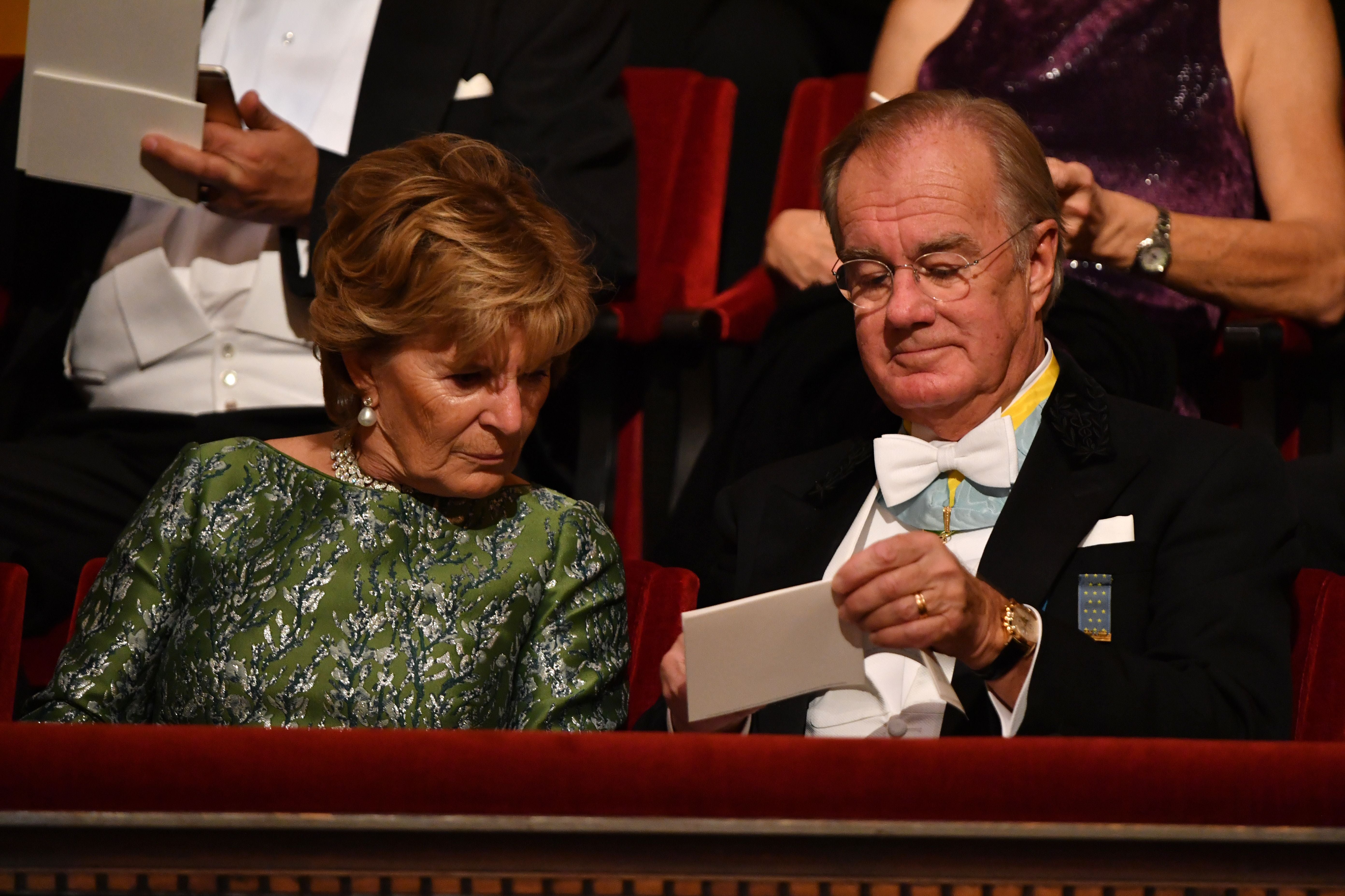Elegantes älteres Paar sitzt bei einer Zeremonie und betrachtet gemeinsam ein weißes Blatt Papier.