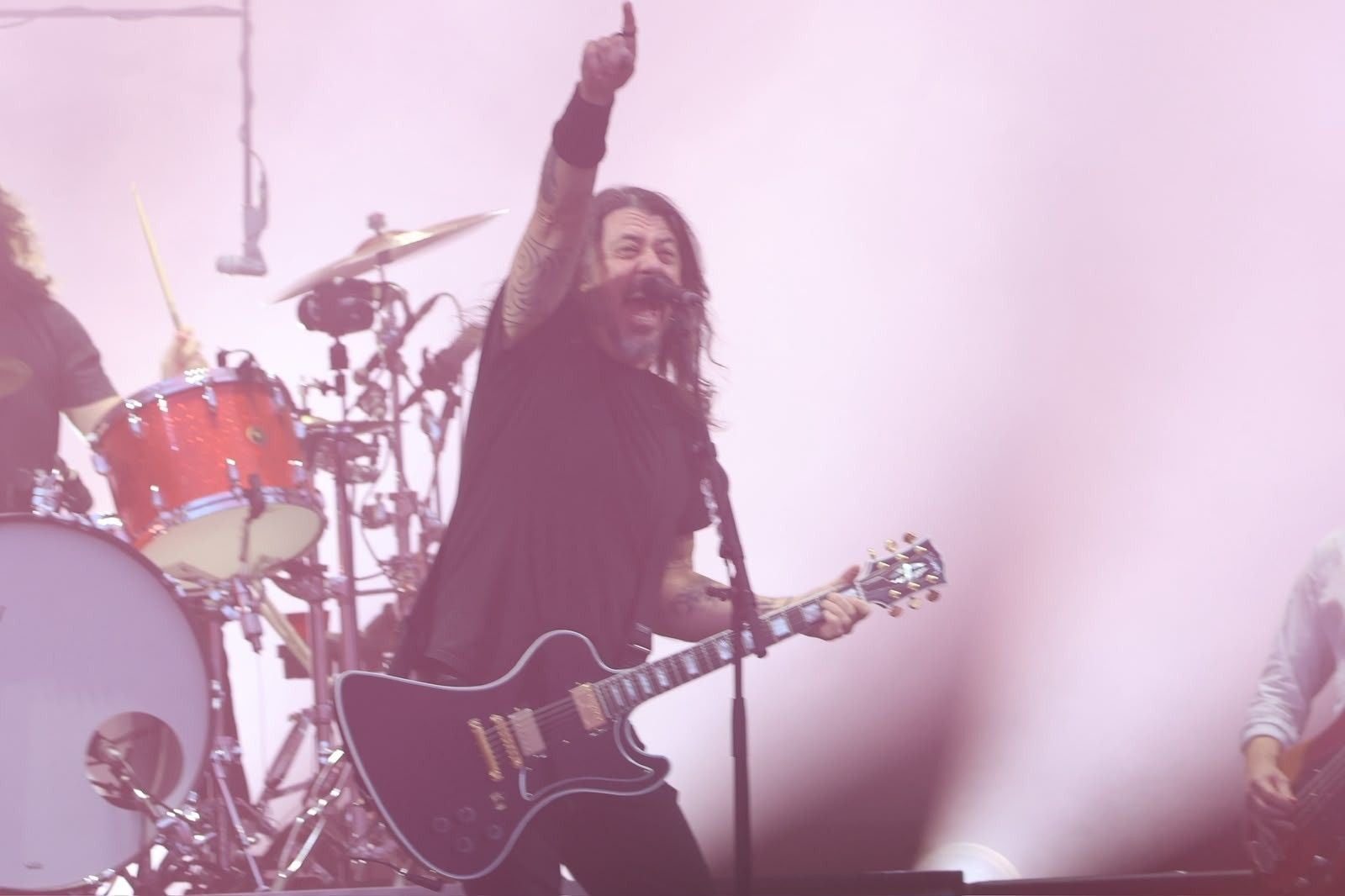 Ein Gitarrist der Band Foo Fighters performt energisch auf einer Bühne mit Schlagzeug im Hintergrund.