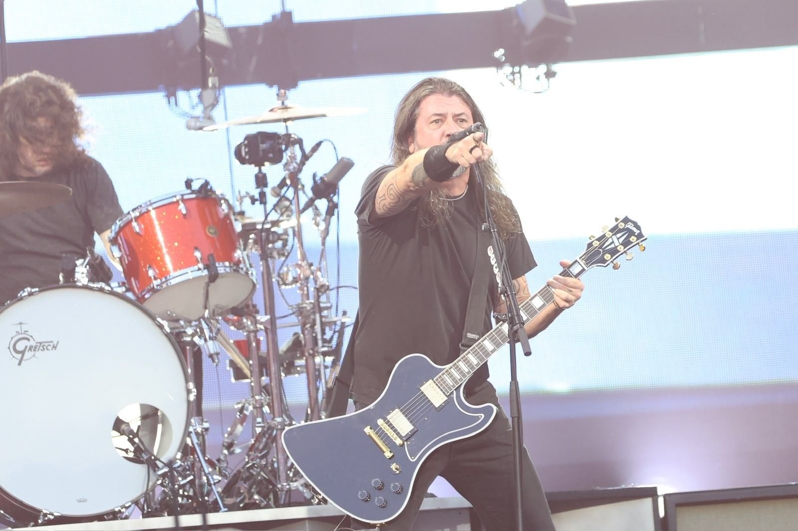 Musiker der Foo Fighters spielt Gitarre und singt auf einer Konzertbühne mit Schlagzeug im Hintergrund.