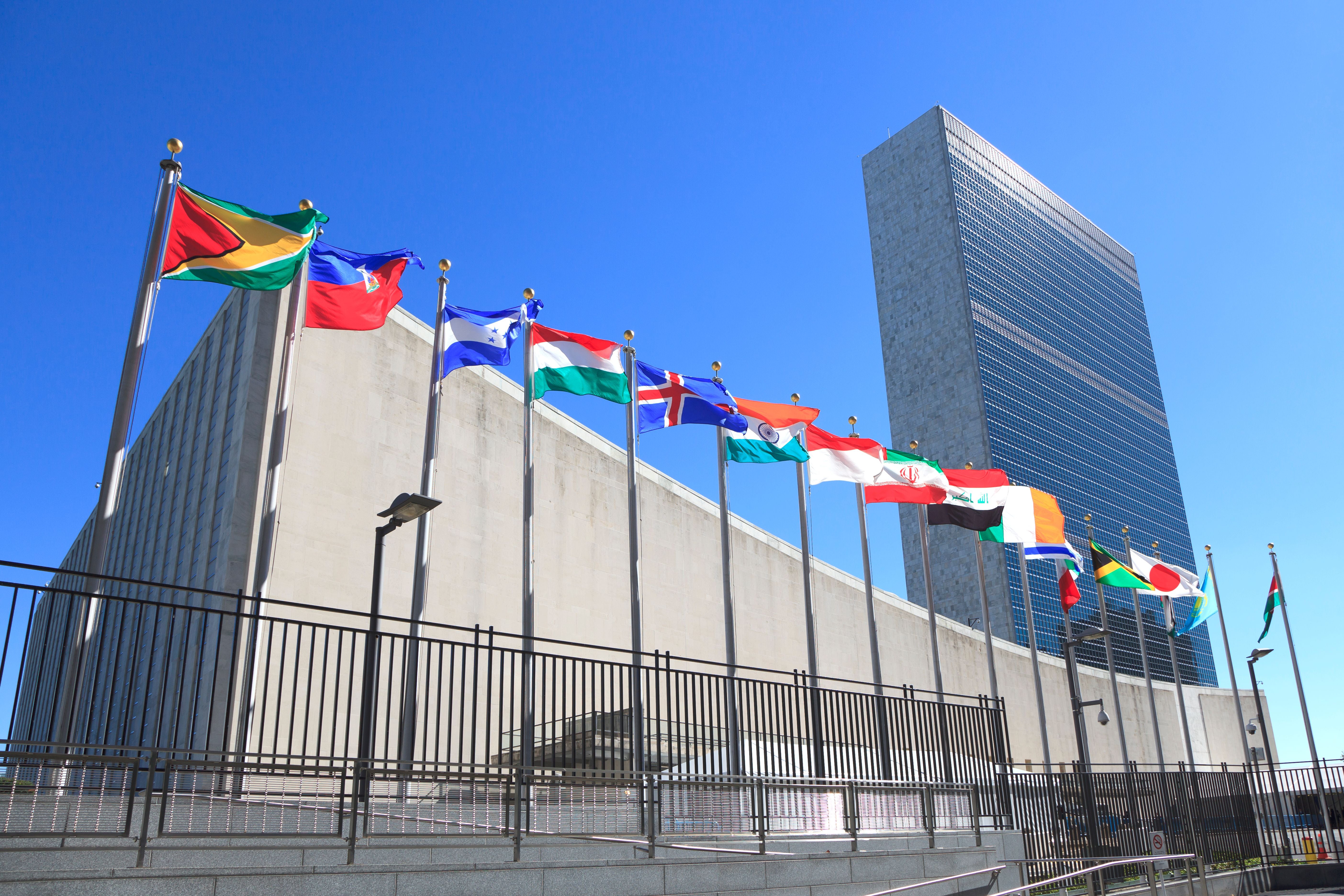 UN-Hauptgebäude mit wehenden Länderflaggen vor blauem Himmel in New York.