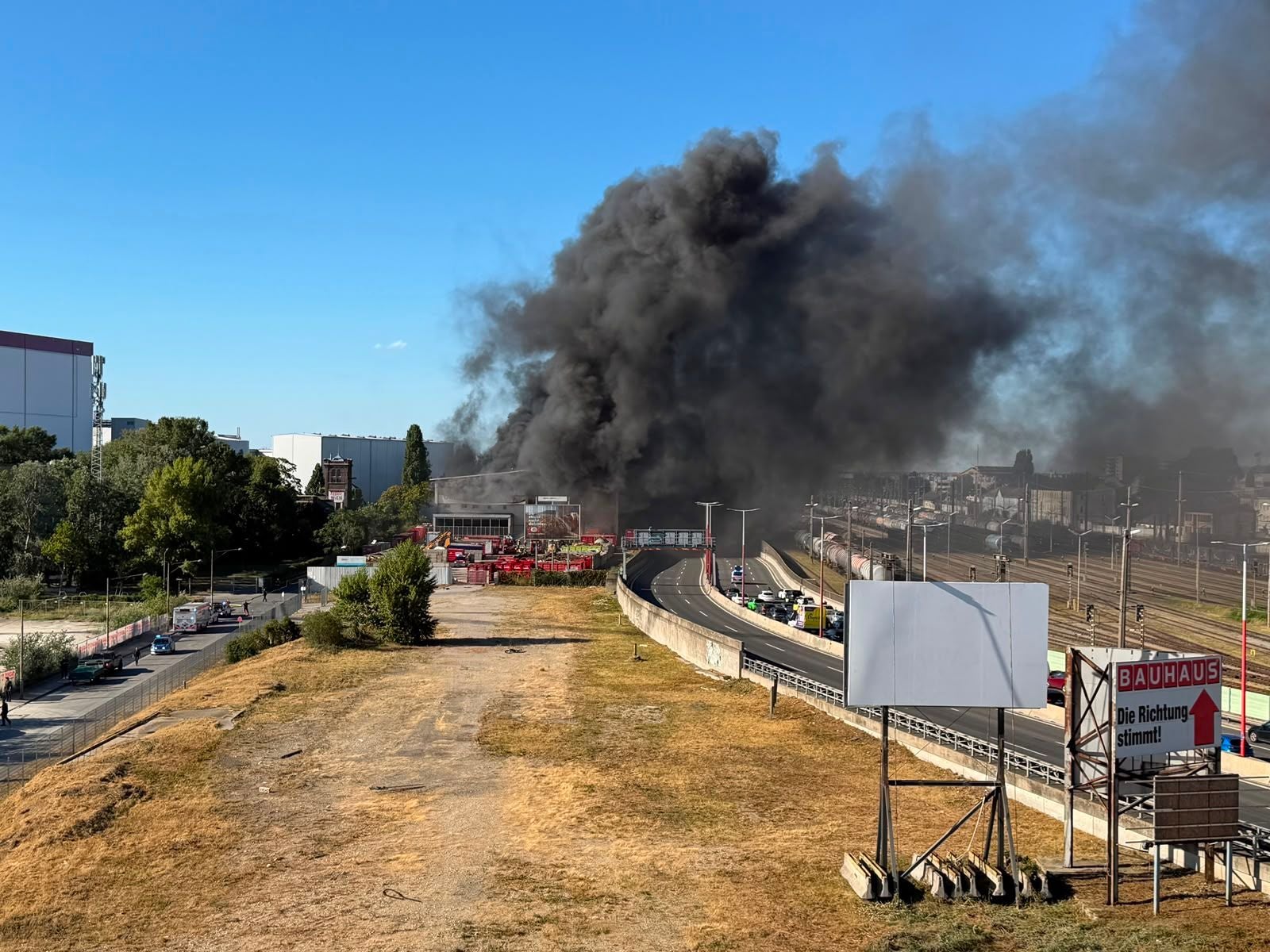 Dichte schwarze Rauchwolke steigt über Gebäuden und Bahngleisen in Stadlau auf.