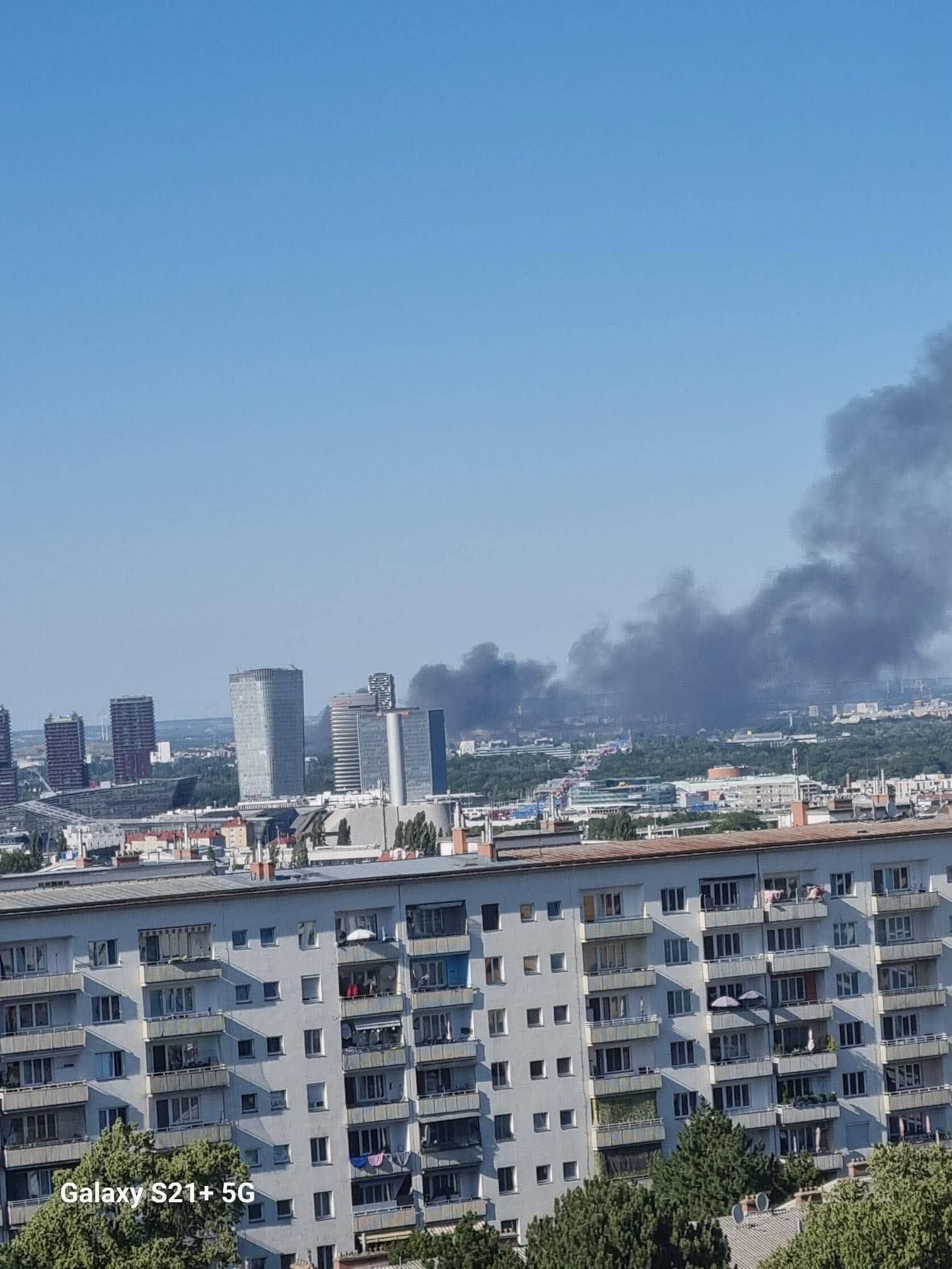 Blick auf Stadlau mit Hochhäusern, im Hintergrund steigt dunkler Rauch in den Himmel.