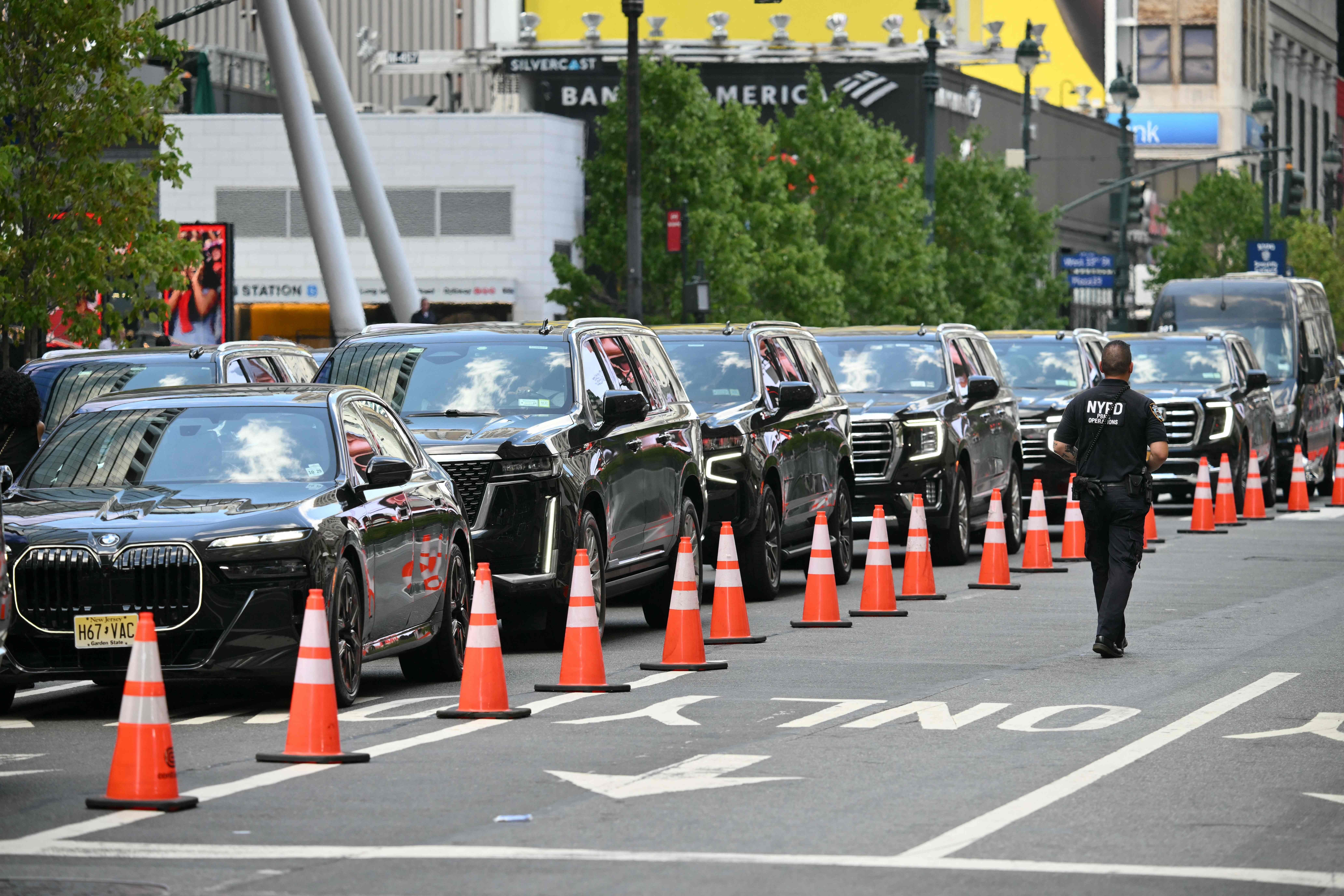 Mehrere schwarze Luxusautos stehen hinter Verkehrskegeln, ein NYPD-Beamter läuft auf der Straße.