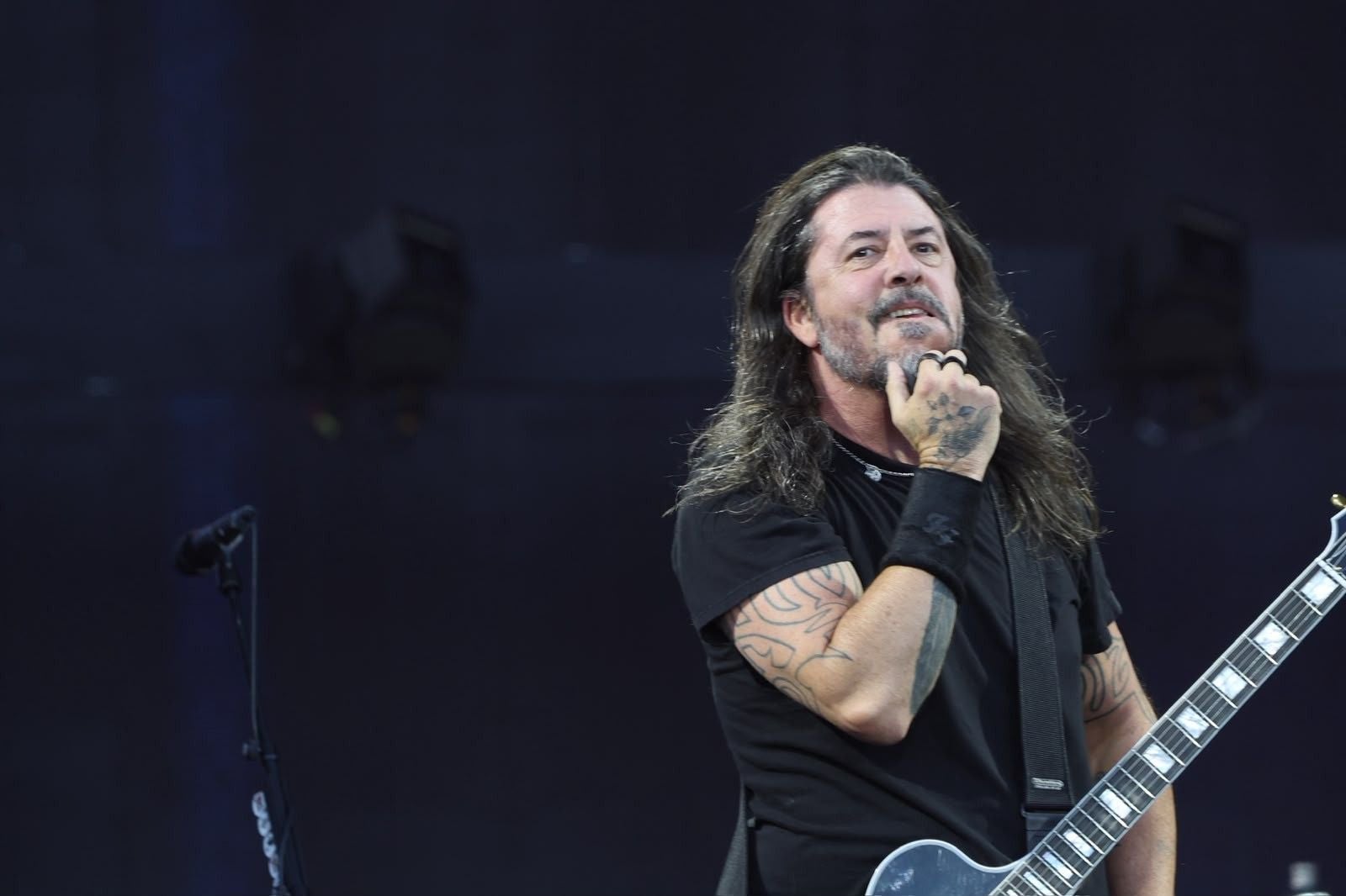 Mann mit Gitarre und Tattoos steht nachdenklich auf einer Bühne bei einem Foo Fighters Konzert.
