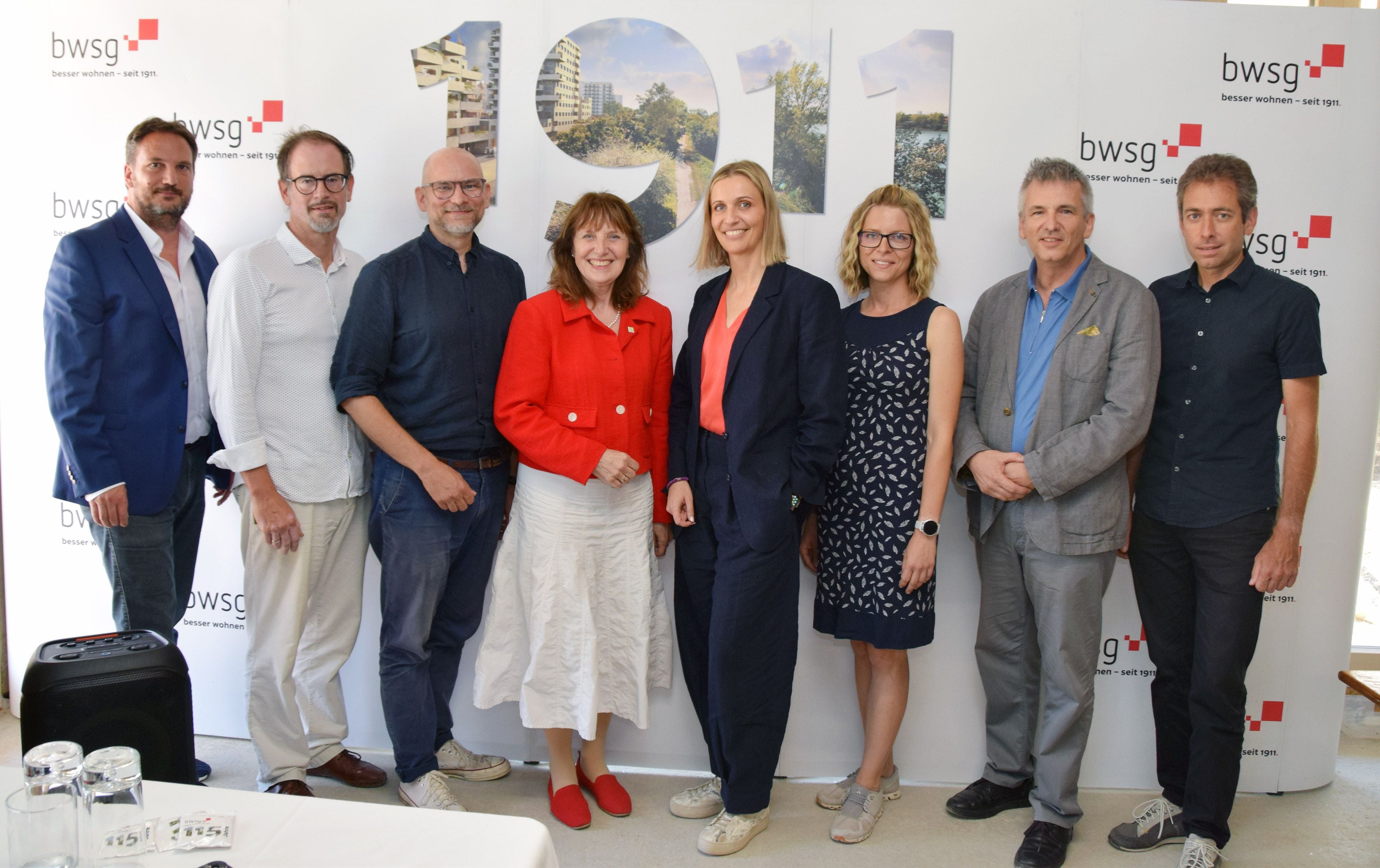 Acht Personen stehen vor einer Wand mit der Aufschrift "1911" und dem Logo der bwsg.