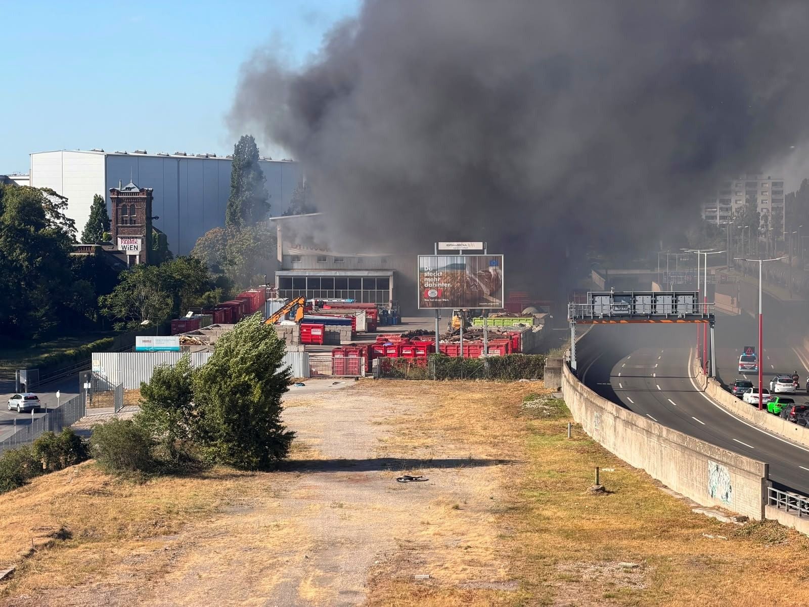 Dichte Rauchwolke steigt von einem Brand auf dem Gelände von brandStadlau neben einer Straße auf.