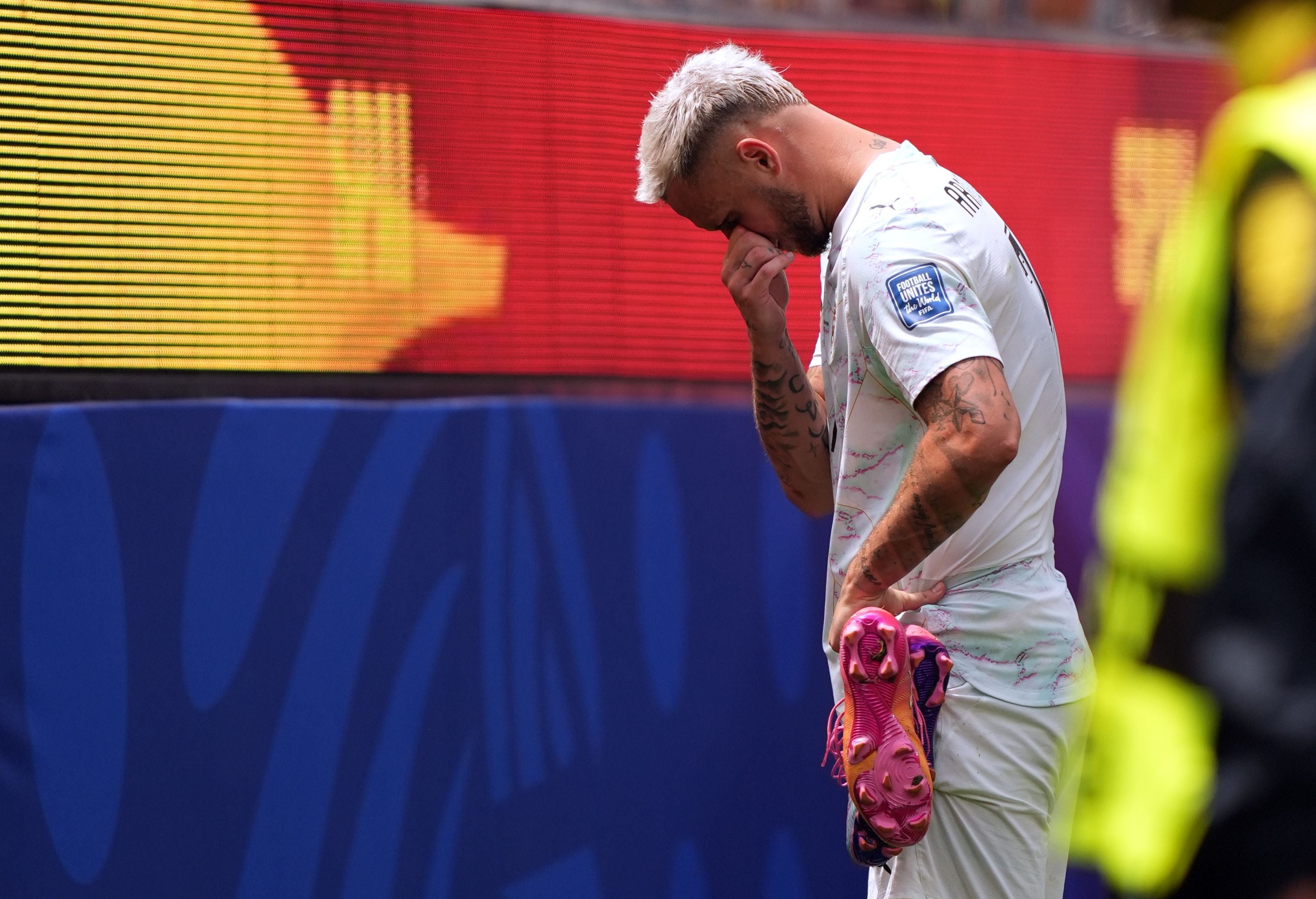 Ein enttäuschter Fußballspieler hält seine Schuhe und verbirgt sein Gesicht nach einem Spiel.