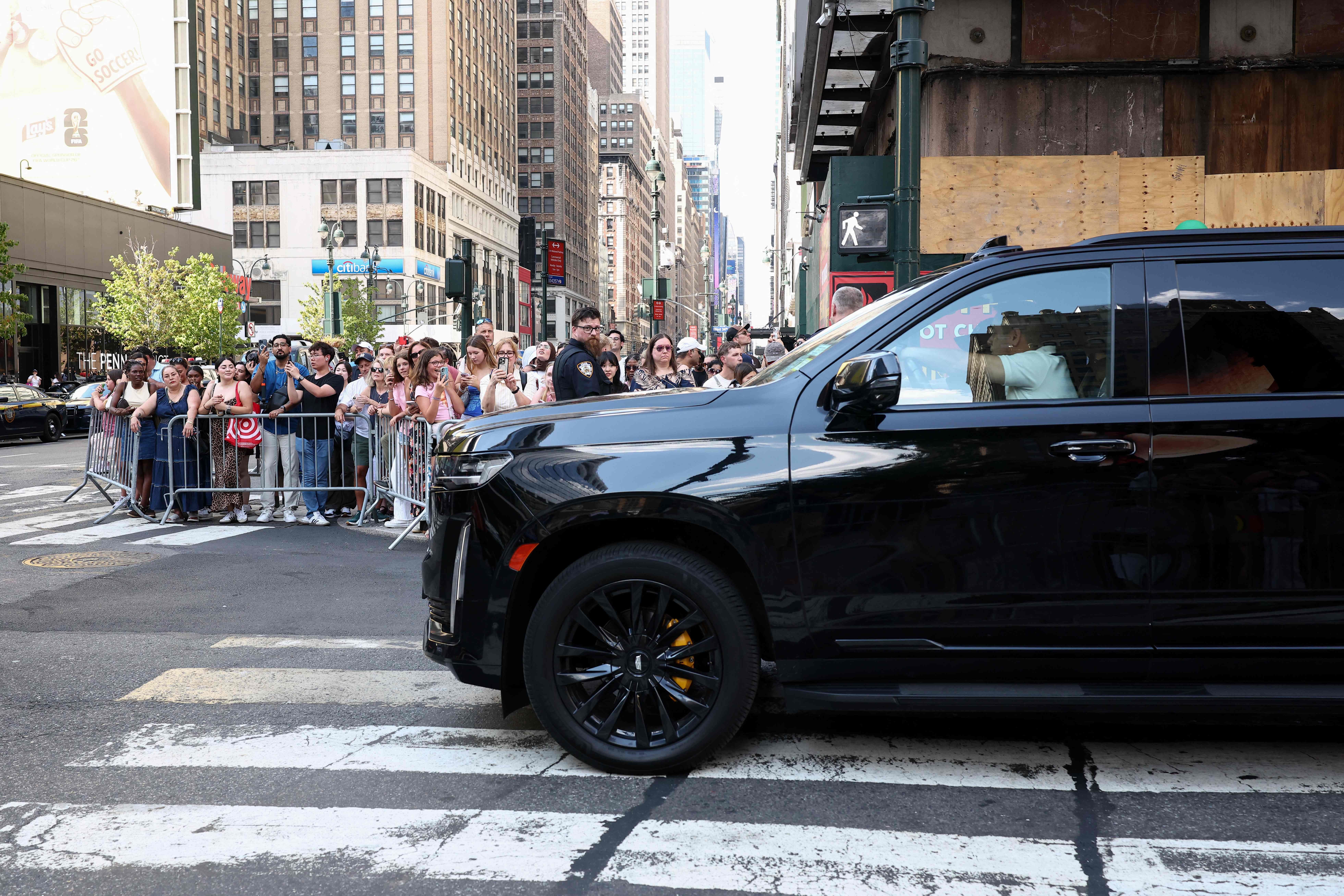 Menschenmengen stehen hinter Absperrungen auf einer Straße in New York neben einem schwarzen SUV.